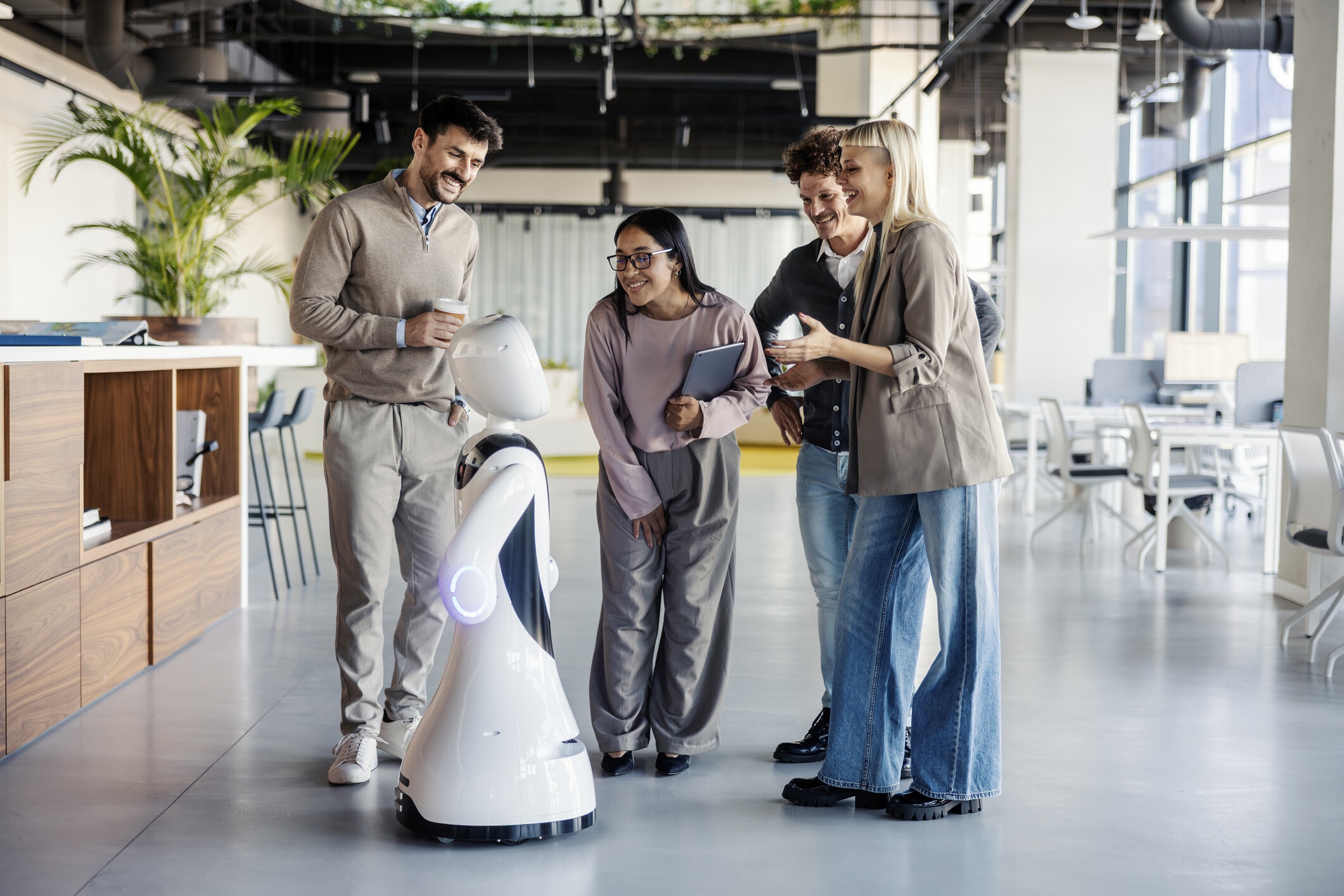 Diverse team of business people standing and smiling, watching a futuristic robot in an innovative workspace, showcasing ai integration: Will the public accept social robots?