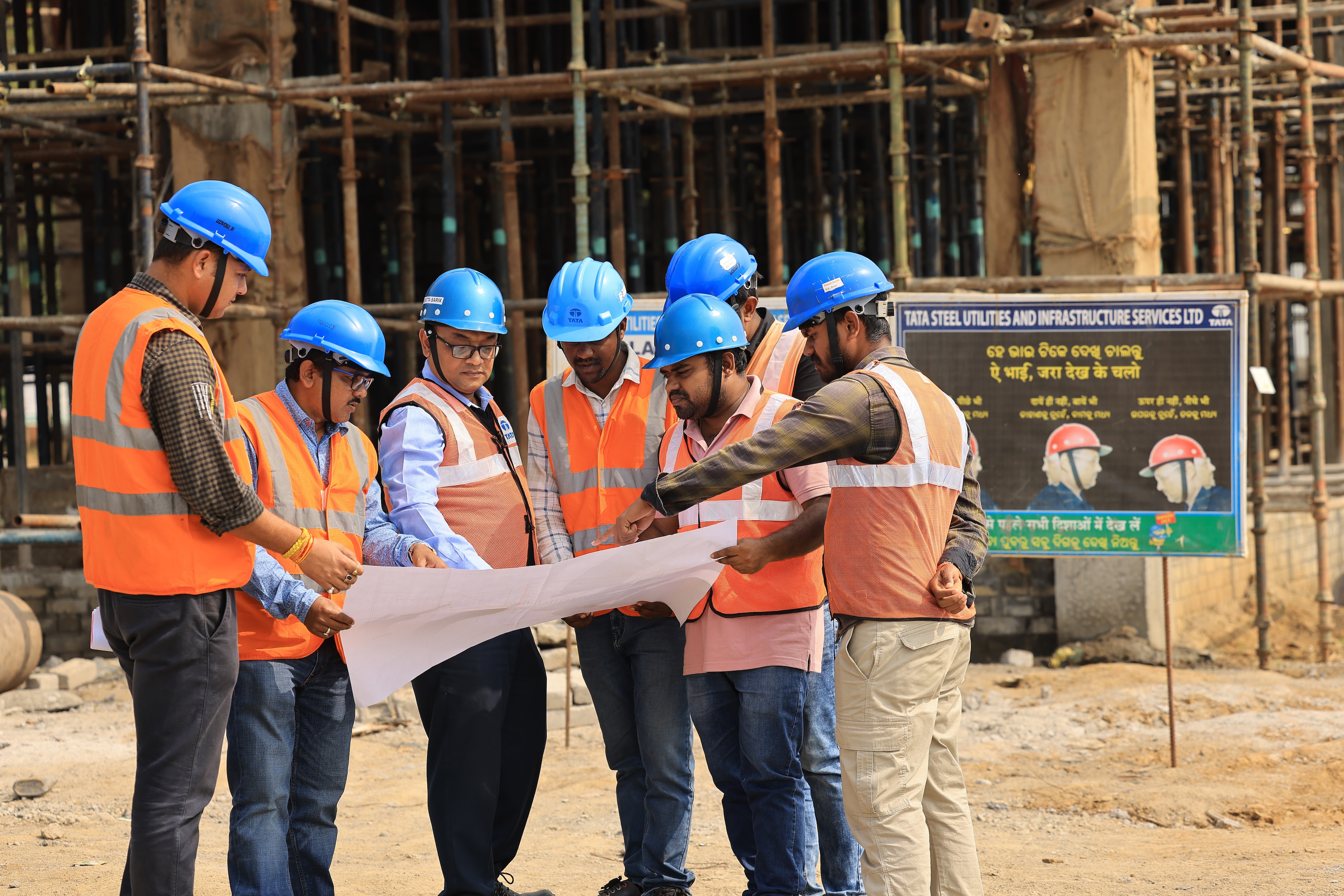 A group of workers in hard hats look at a plan on a building site; clean energy; India