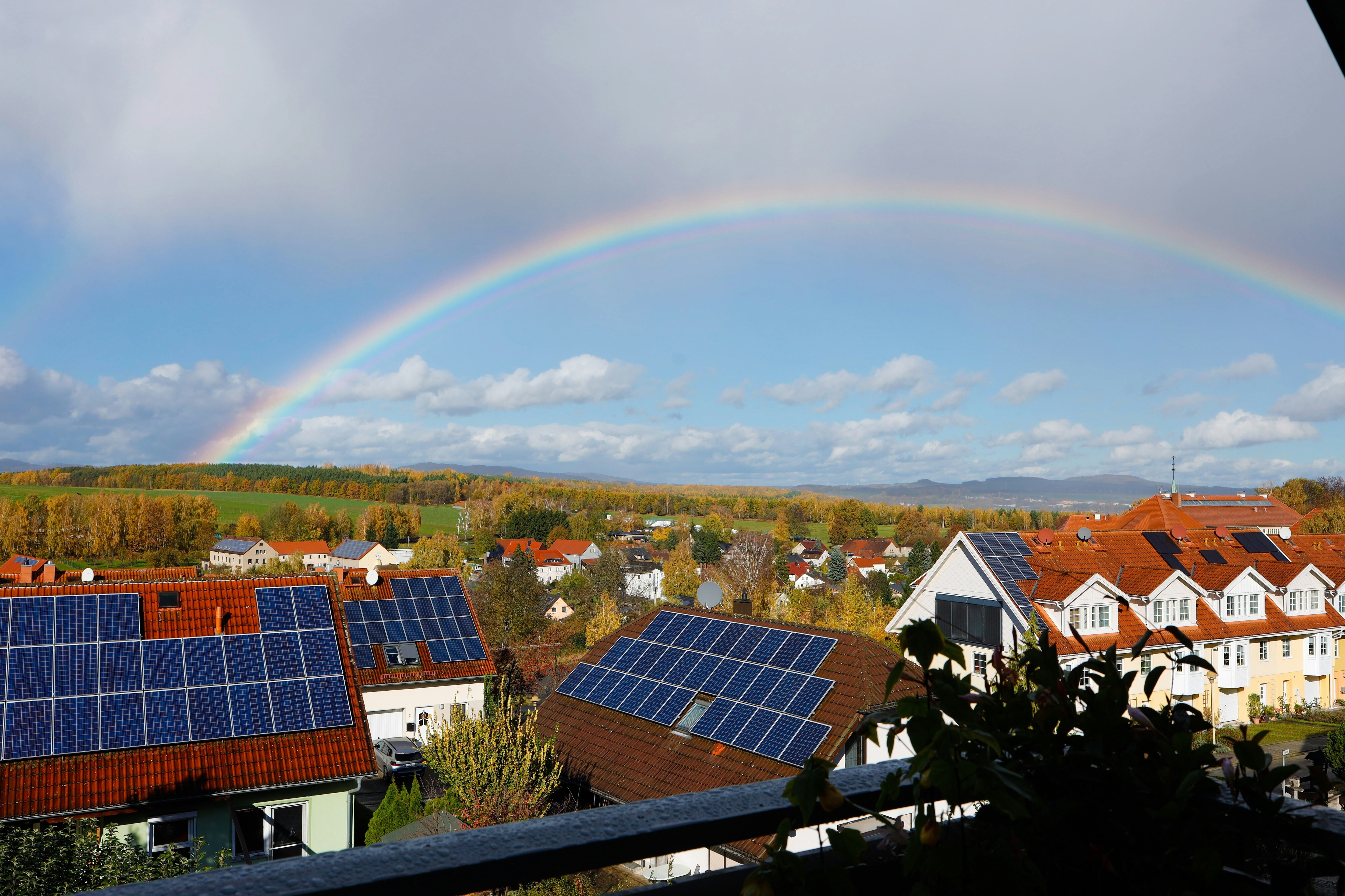 Houses with solar panels on the roof and a rainbow in the background.