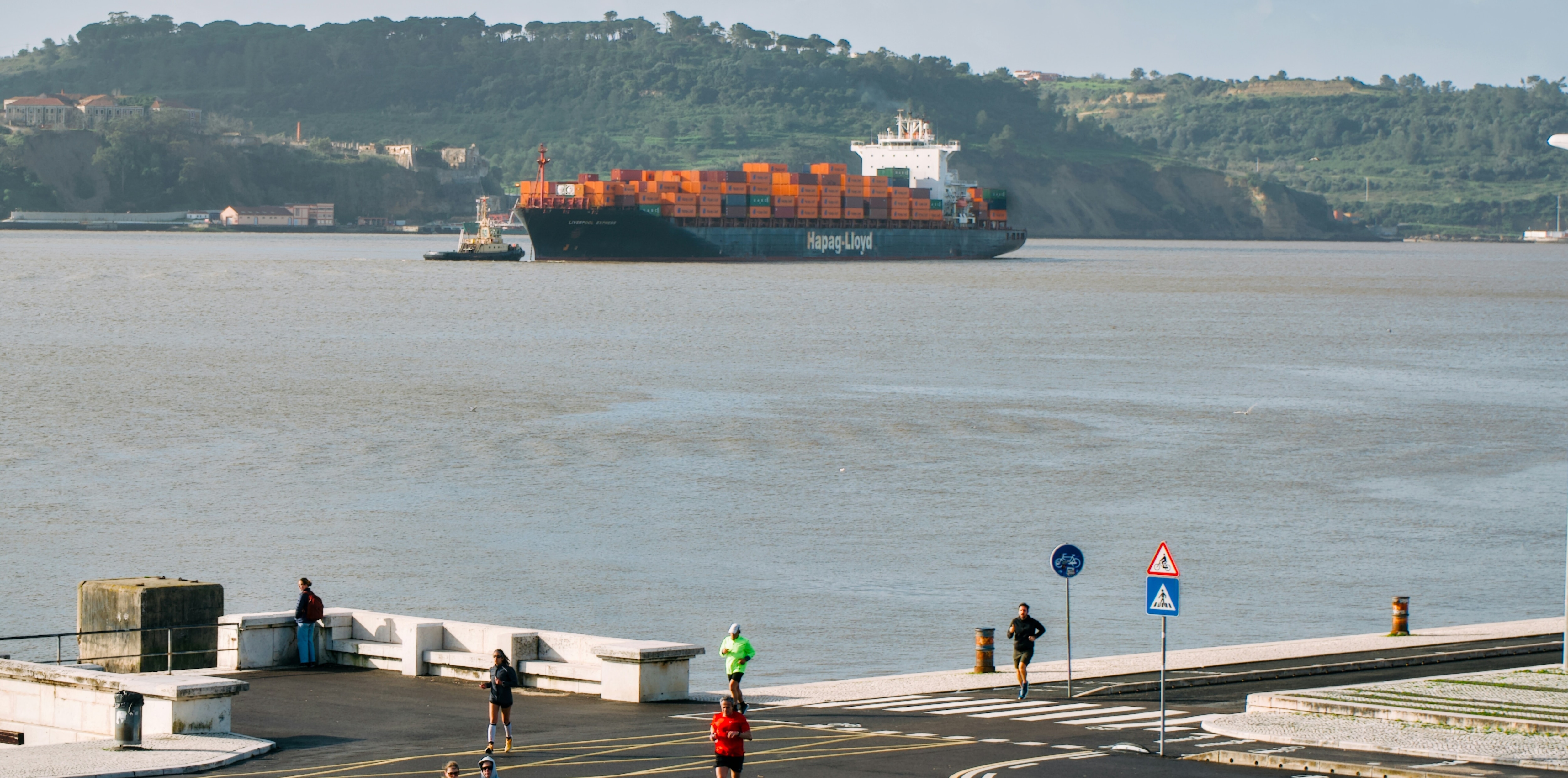 Cargo ships sails on a wide river near a town with people running in sight: The trade financing gap is rising despite underlying trade being stable