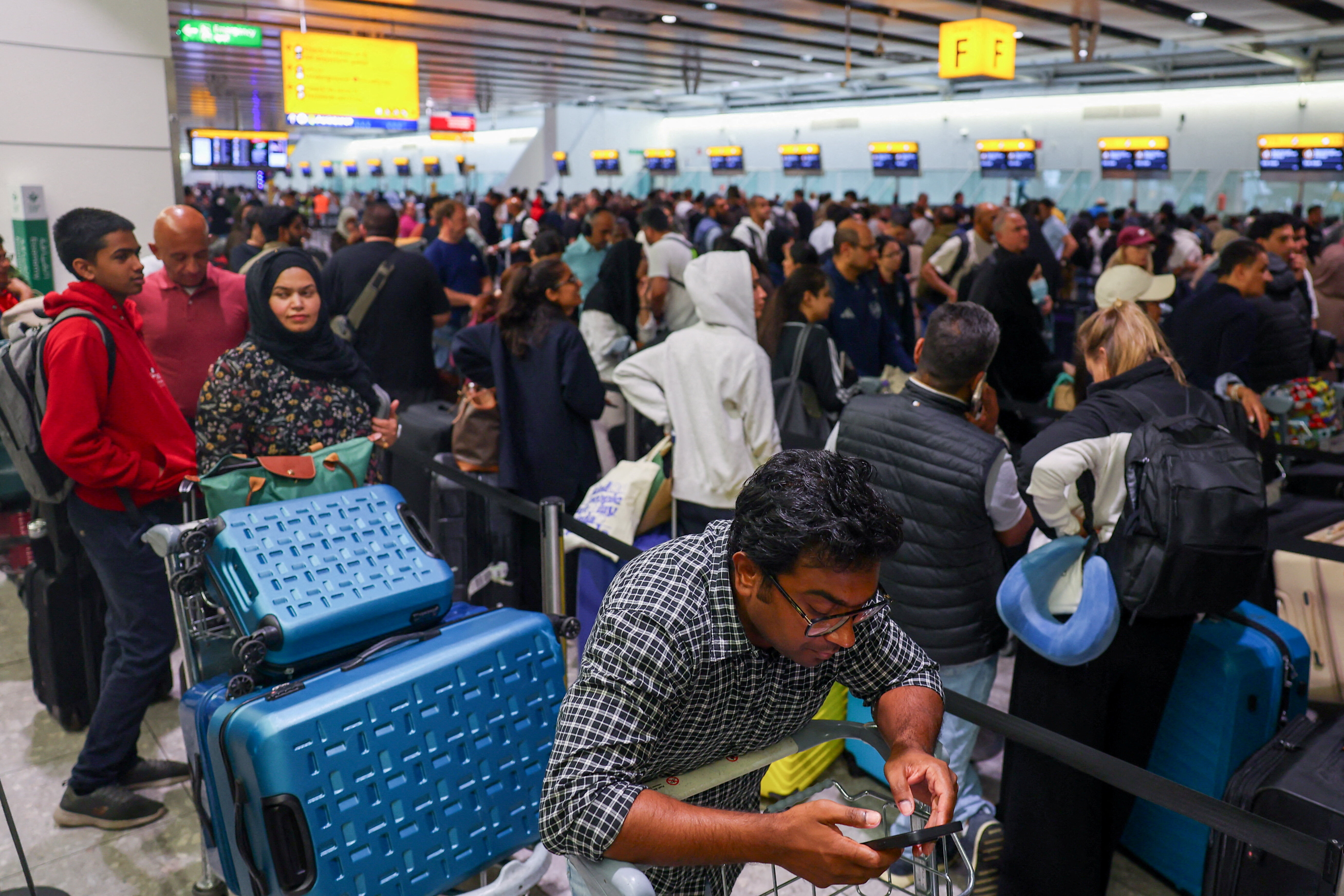 A man uses a smartphone as travellers queue to check in at Heathrow Airport Terminal 4, following a disruption to check-in and boarding systems caused by a cyber attack which has affected several major European airports, resulting in flight delays and cancellations, in Greater London, Britain, September 20, 2025. REUTERS/Isabel Infantes/File Photo