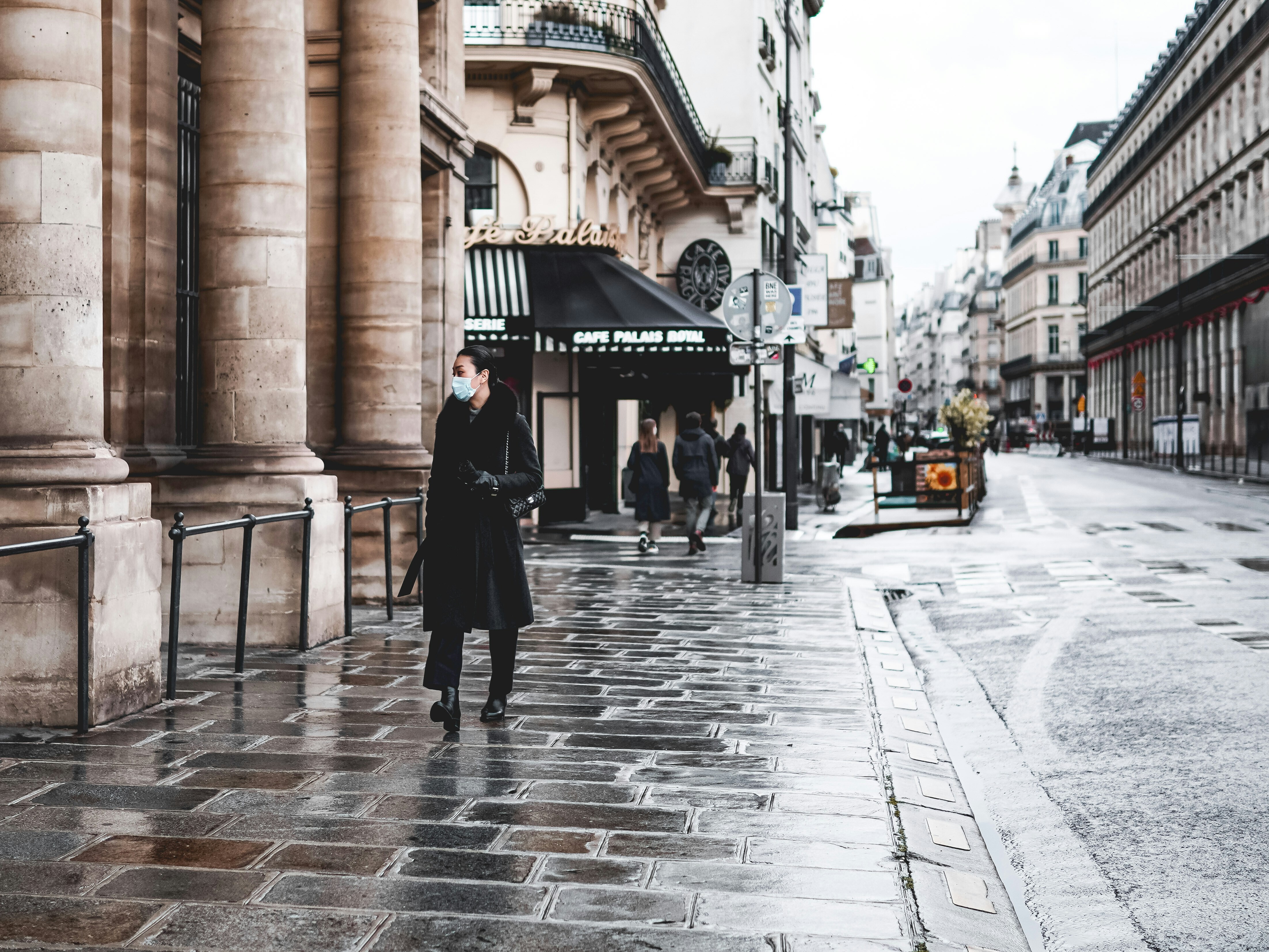 A lady wearing a medical mask walking through the streets of Paris.