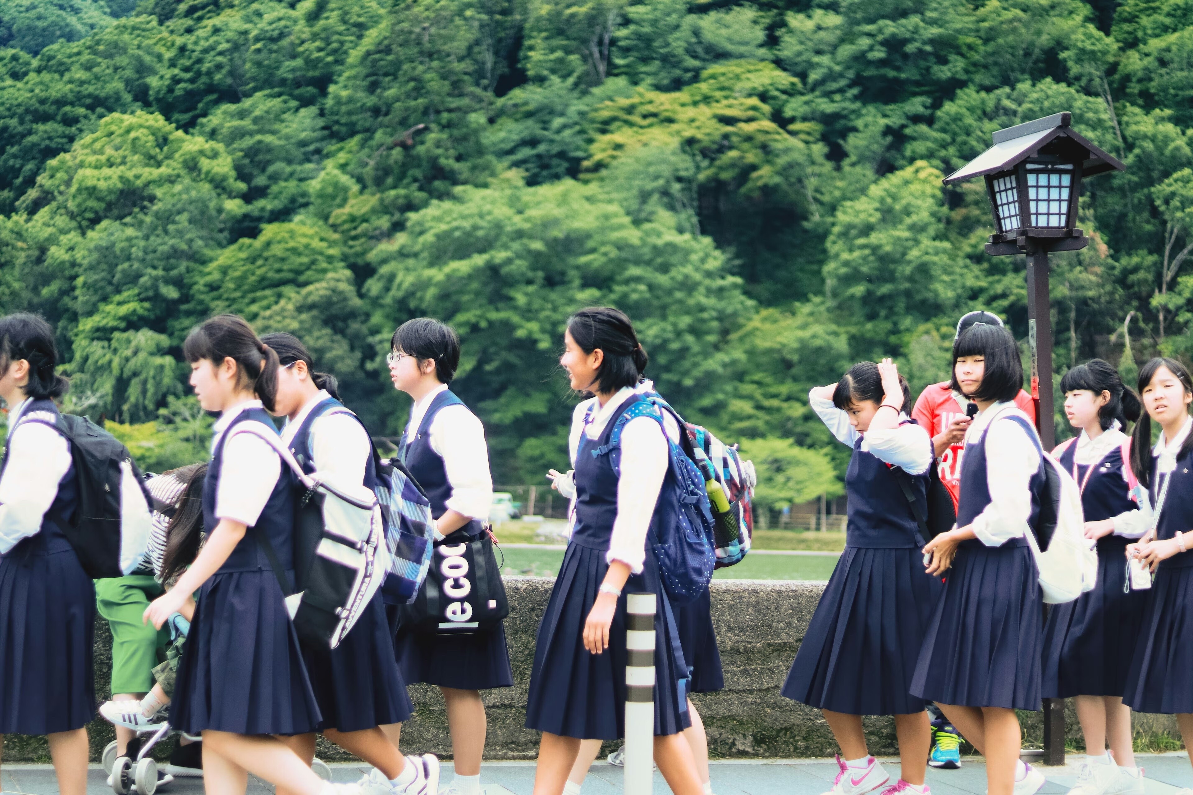 Niños con uniformes escolares y mochilas, árboles verdes; educación financiera, Japón.
