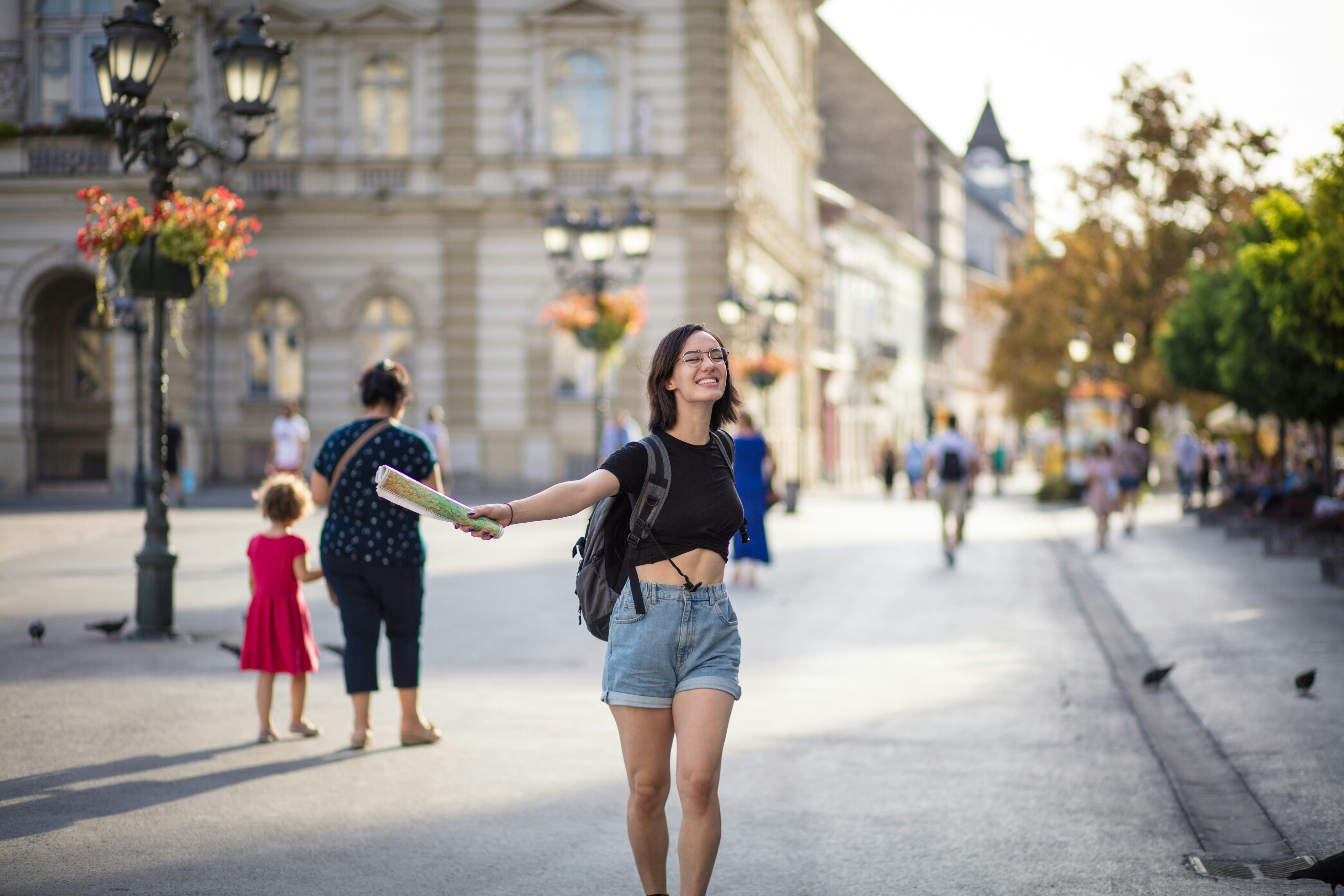 A happy woman in demim shorts a t-shirt is pouncing gleefully forward with a street-level city backdrop: The ‘experience dividend’ kicks in when a city or area offers a better experience for residents and workers