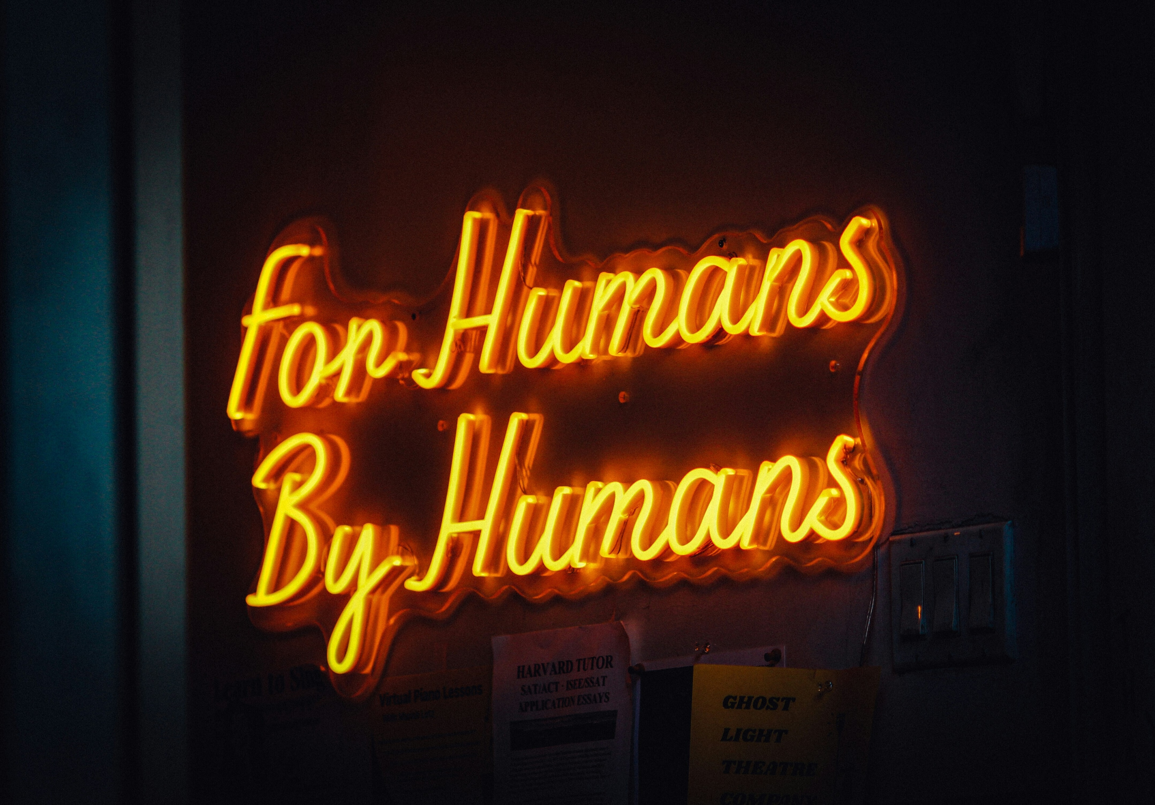 A neon sign reading "For Humans By Humans": Human-first AI must come from a whole of society approach.