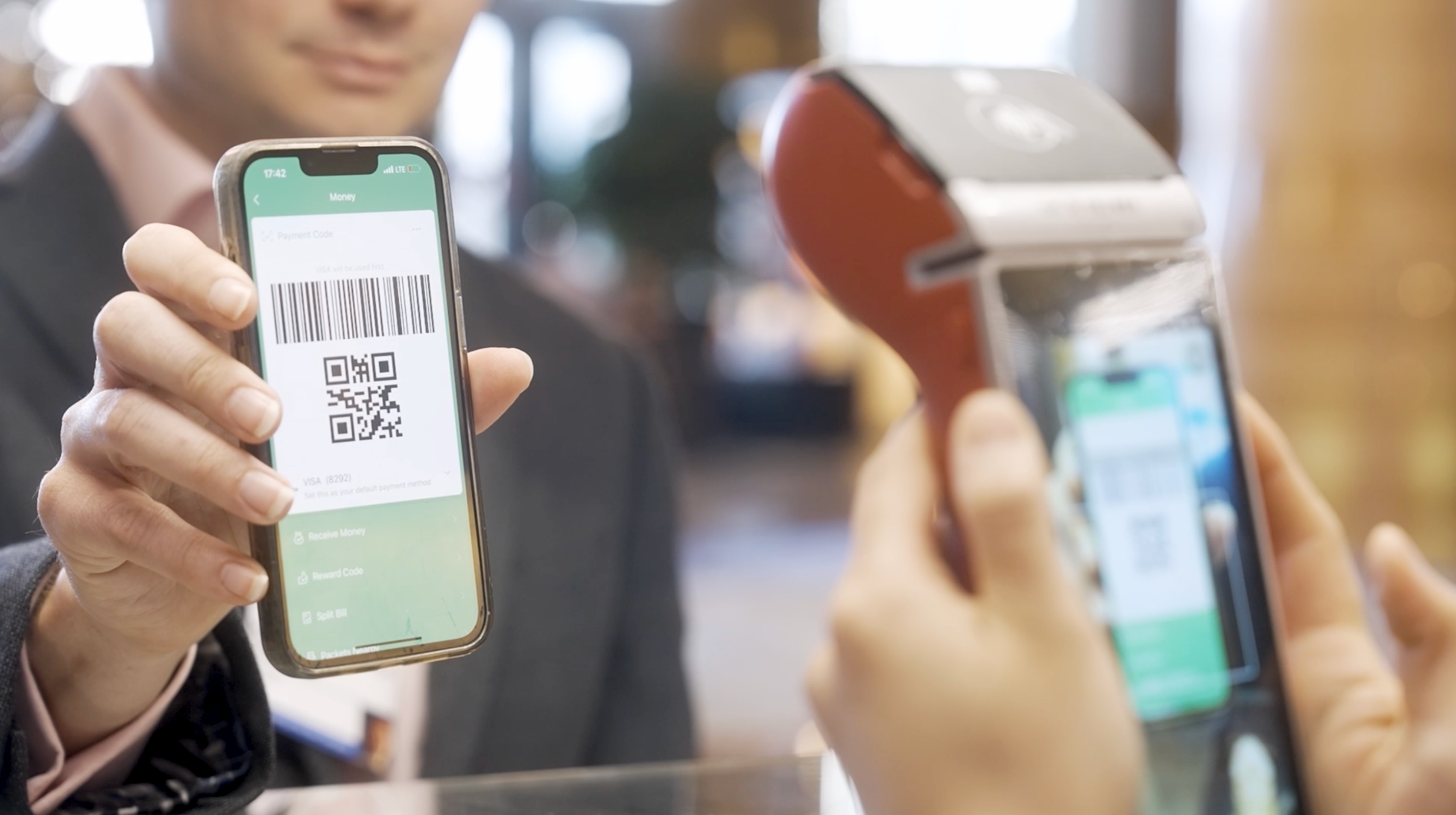 A man in a suit pays using a QR code on the mobile phone he is holding up to a terminal: Interoperability could be the next step towards seamless cross-border payments
