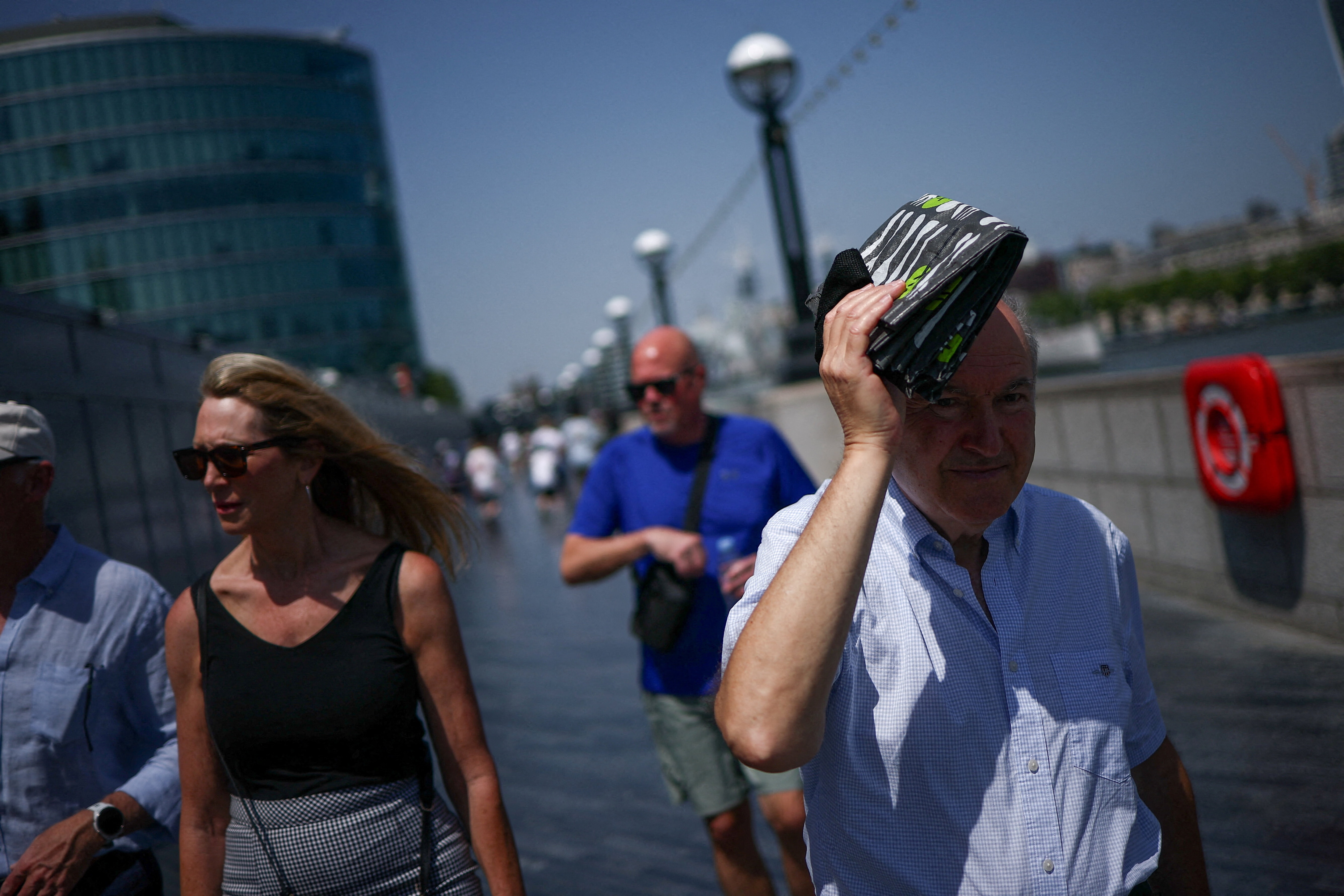 A man uses a shopping bag to shade his face while walking in London during the recent heatwave, highlighting the importance of urgent climate action. 