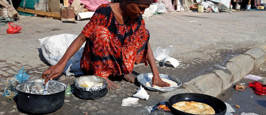 A woman displaced by the war in Yemen cooks on a street in Hodeida