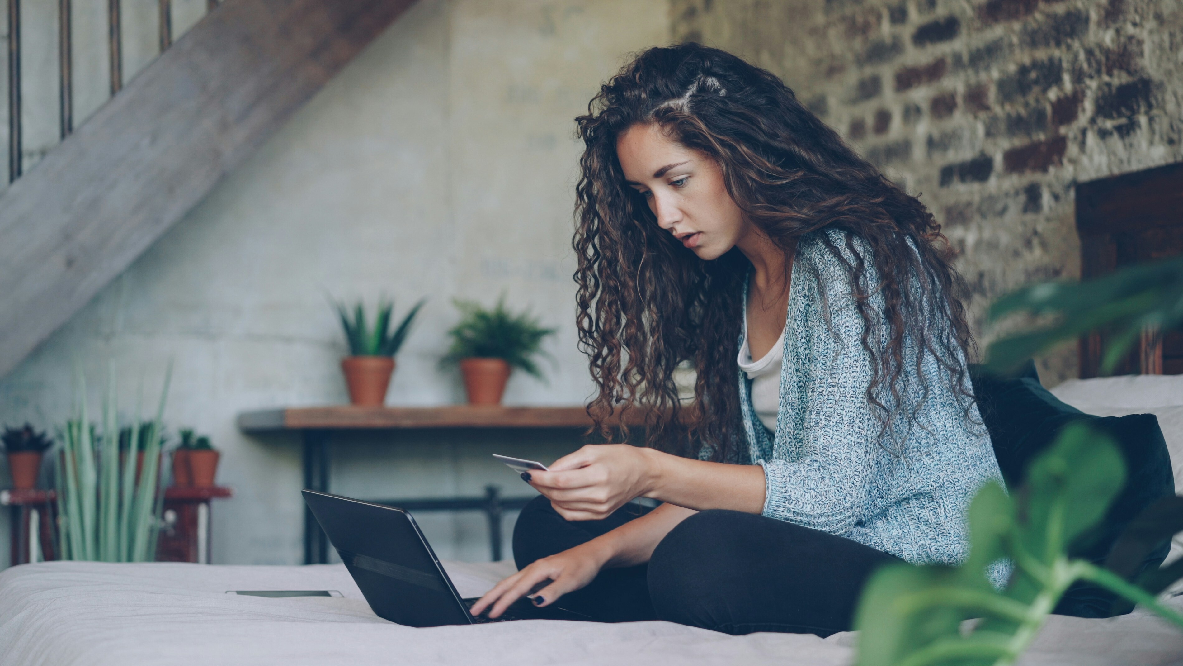 A woman looks at a computer screen while holding a credit card.