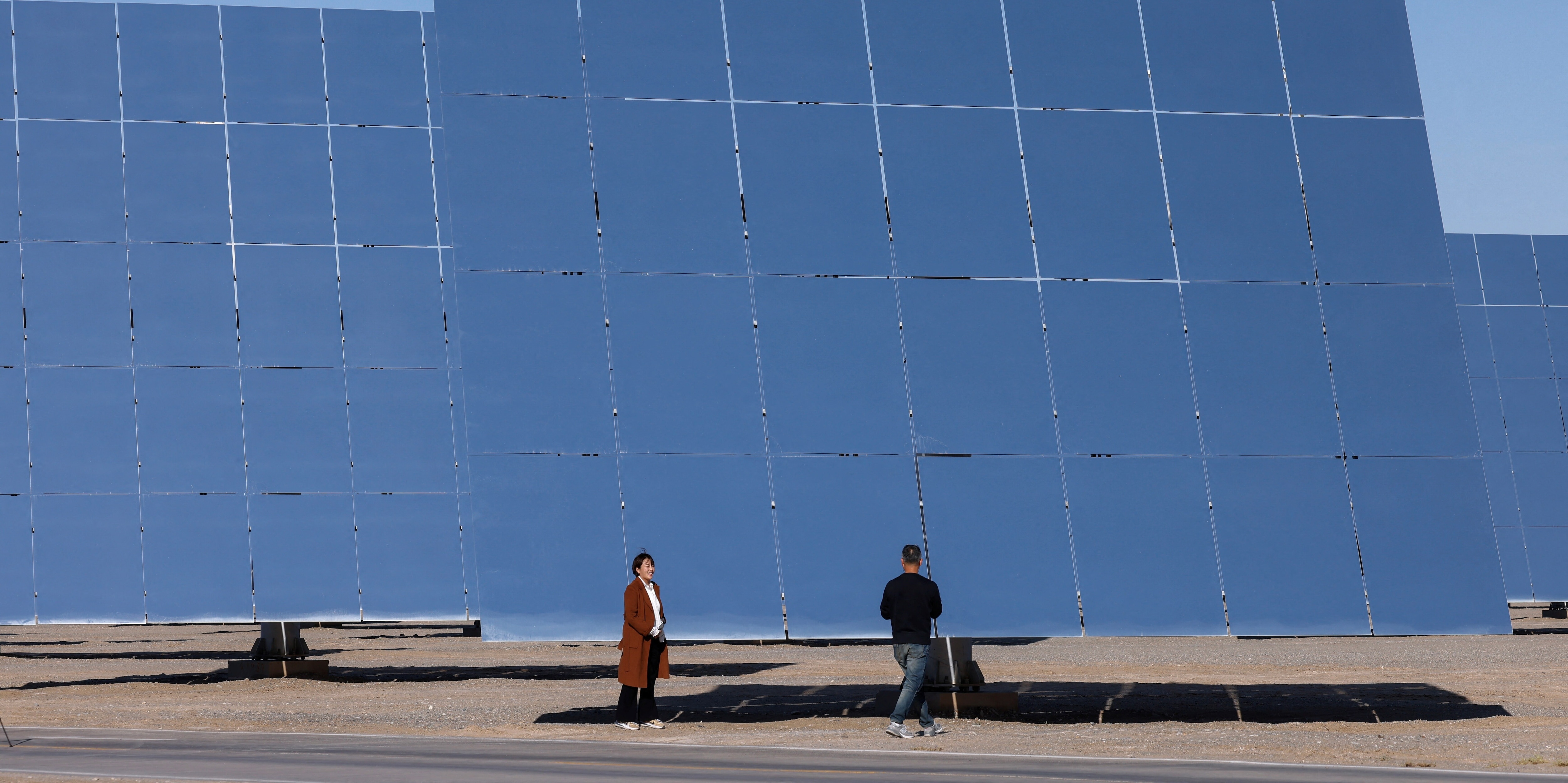 Journalists work next to heliostat mirrors at the site of Dunhuang Shouhang 100MW Tower Solar Thermal Power Generation Project, during an organised media tour to Dunhuang Photovoltaic Industrial Park, in Gansu province, China October 16, 2024. 