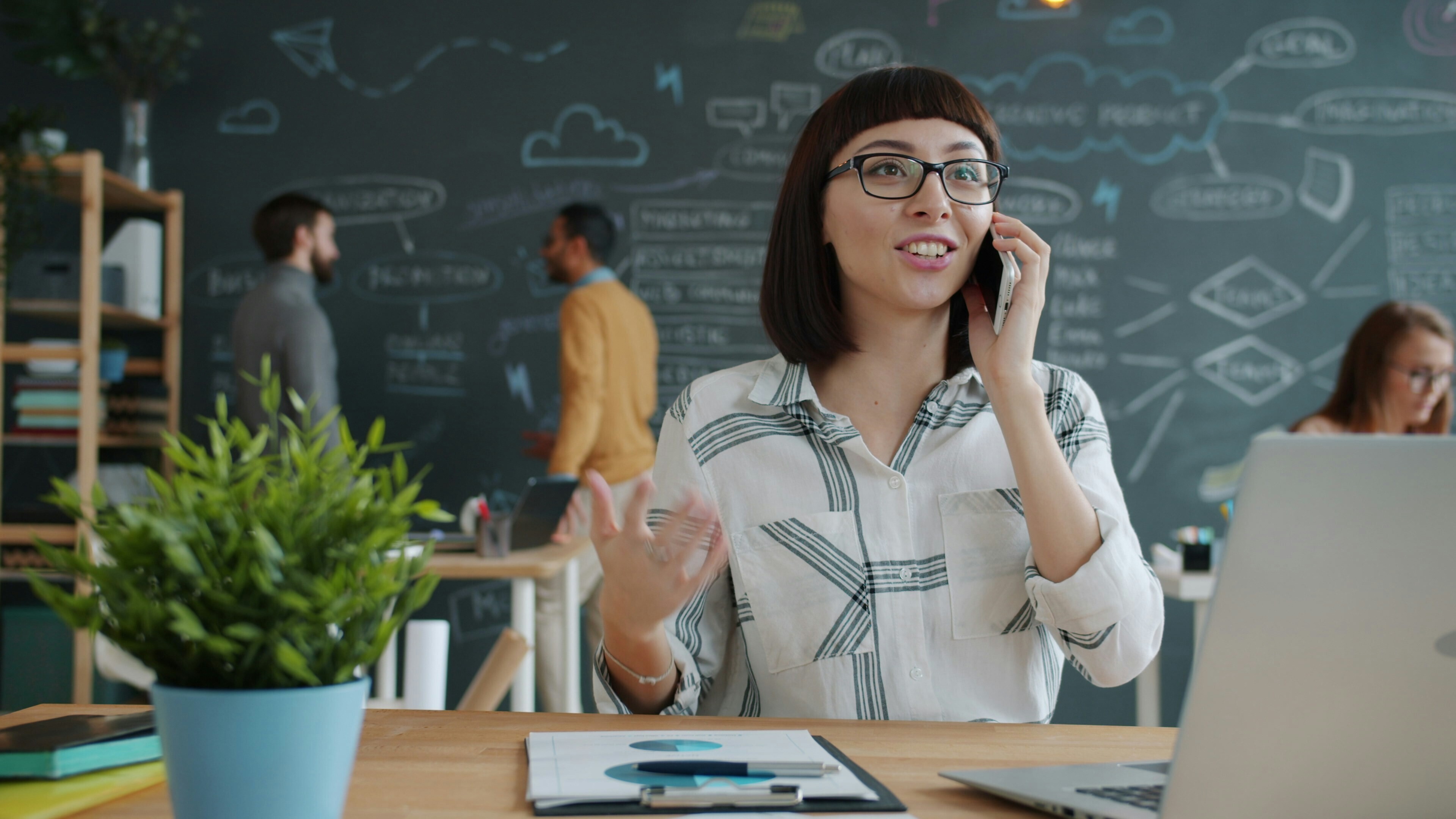 Woman talking on phone in modern office with chalkboard wall. sustainability