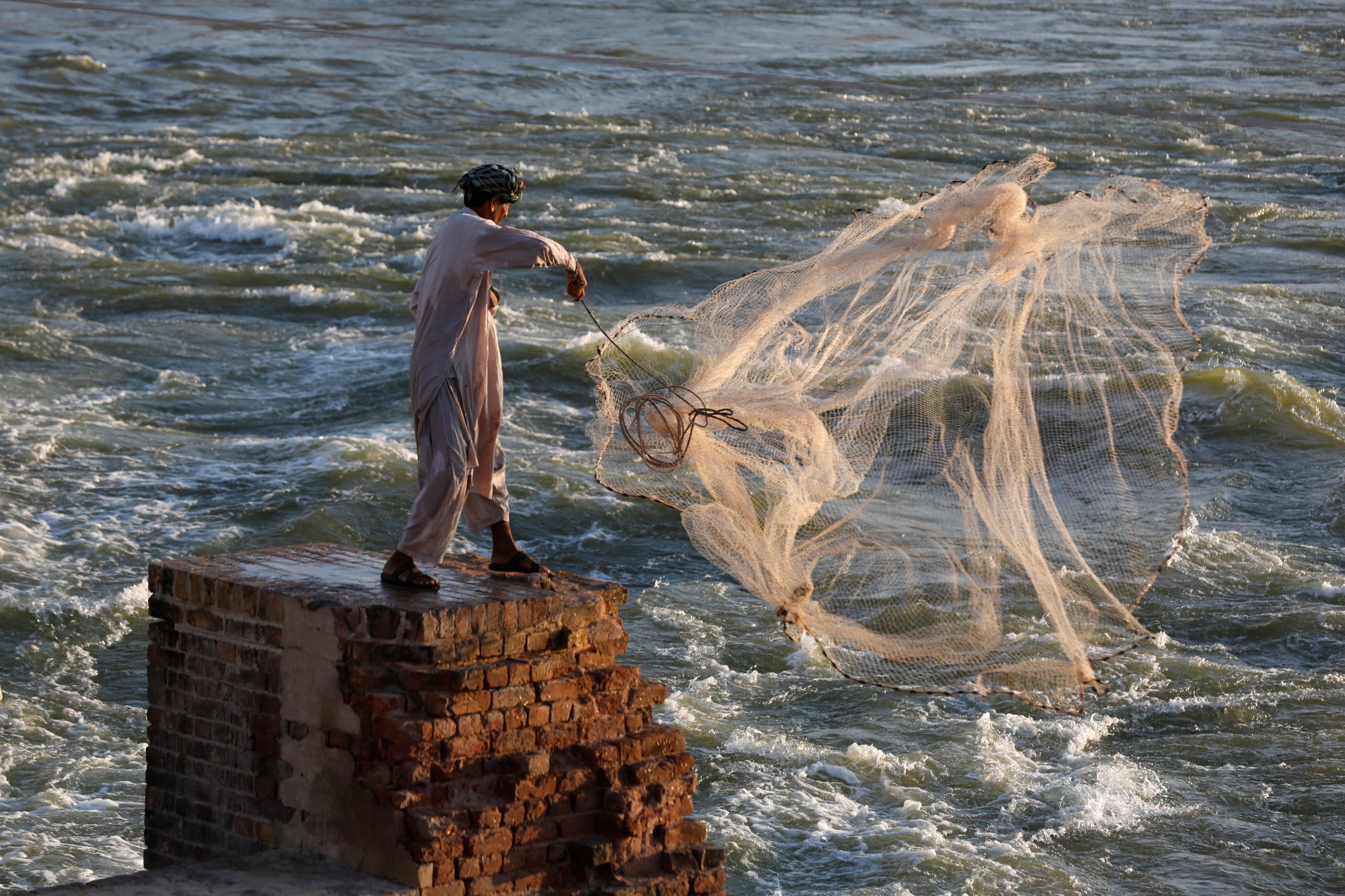 A man displaced during the 2022 Pakistan floods casts a net to catch fish from the flow of floodwaters.