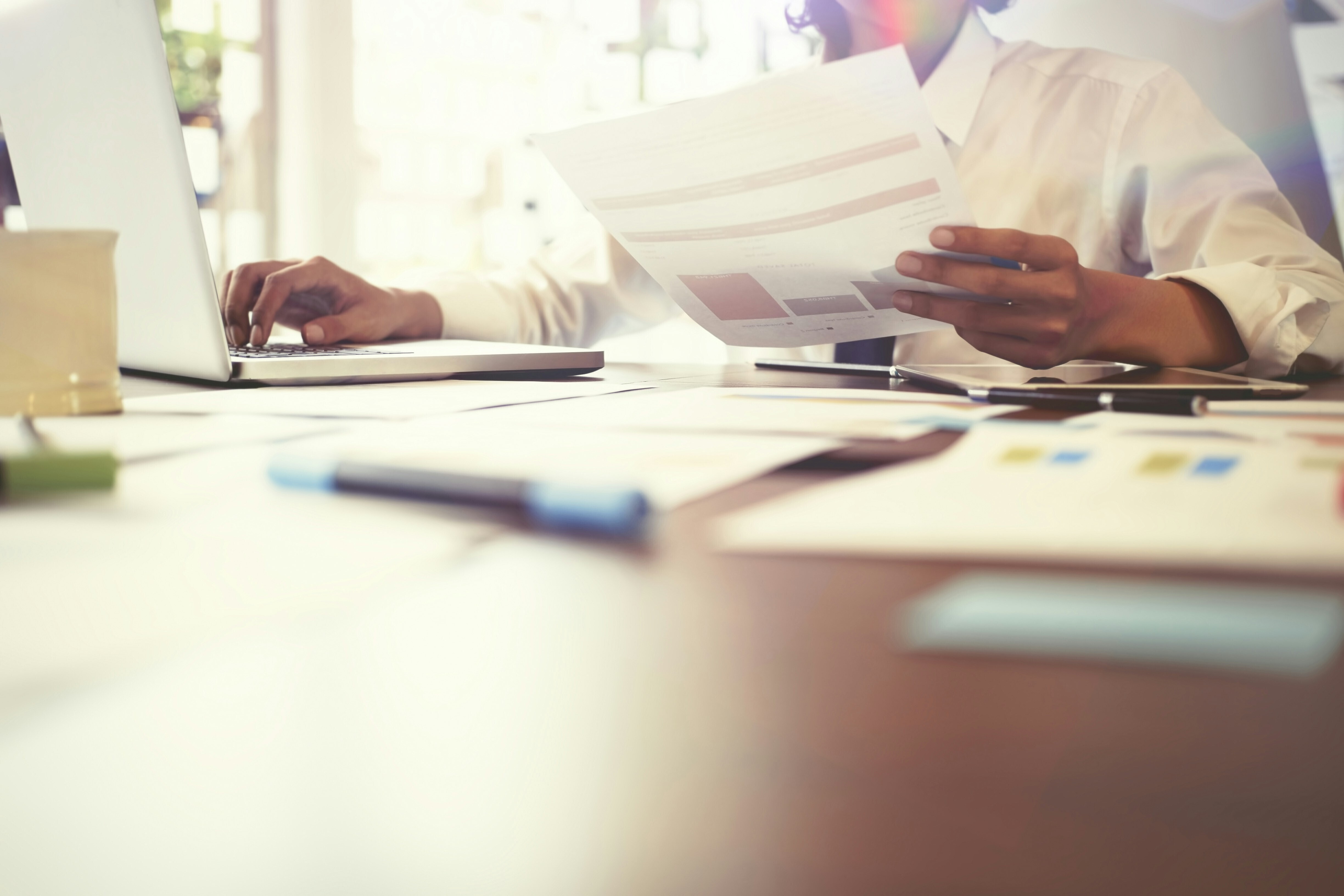 Someone in a white shirt looks at papers while tapping on a laptop: Stress intelligence is becoming an essential and strategic leadership capability
