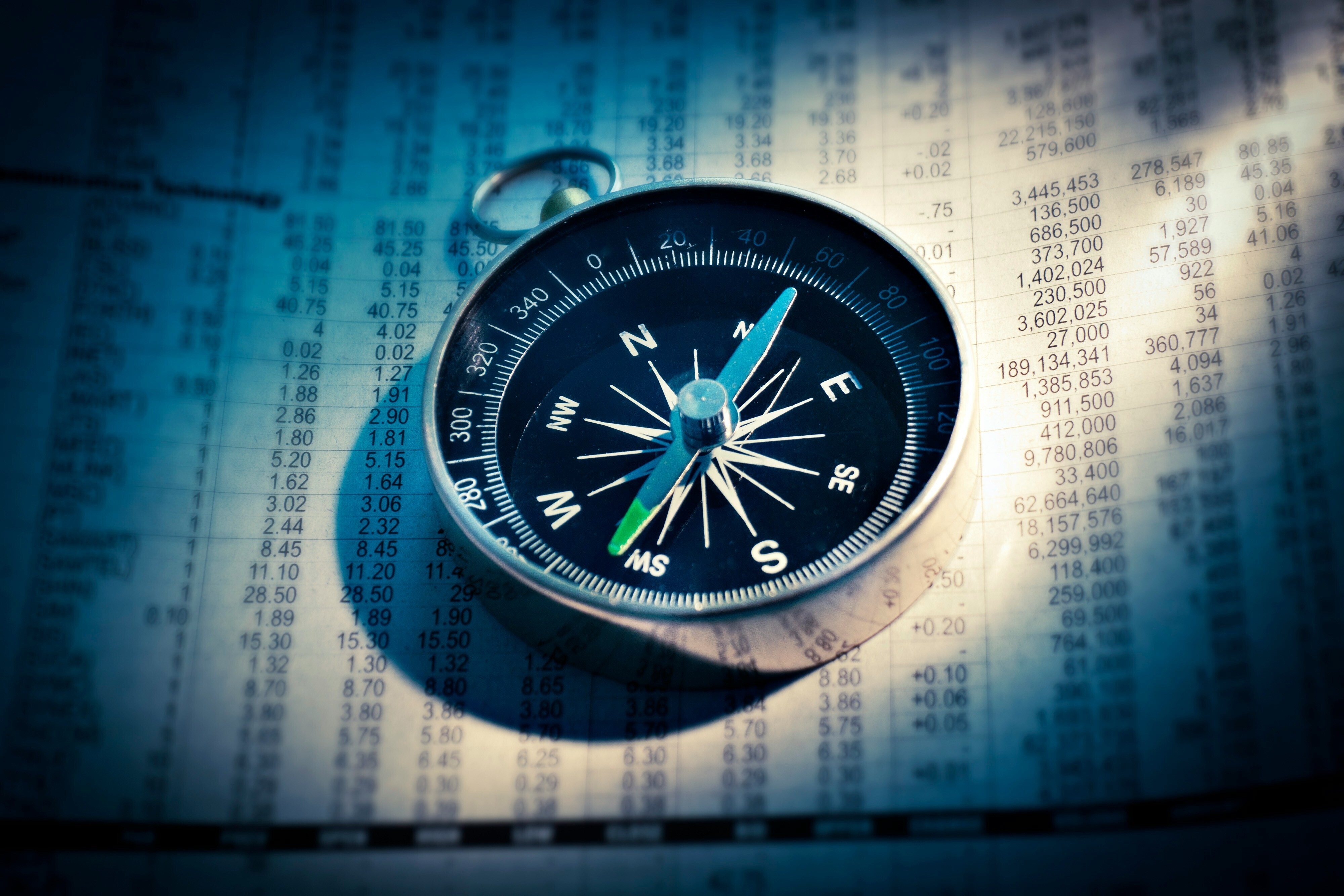 A compass is seen on top of a newspaper with stock market information.