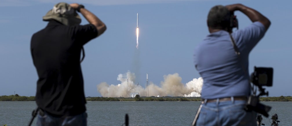 Photographers take pictures of the unmanned SpaceX rocket as it launches from Cape Canaveral, Florida