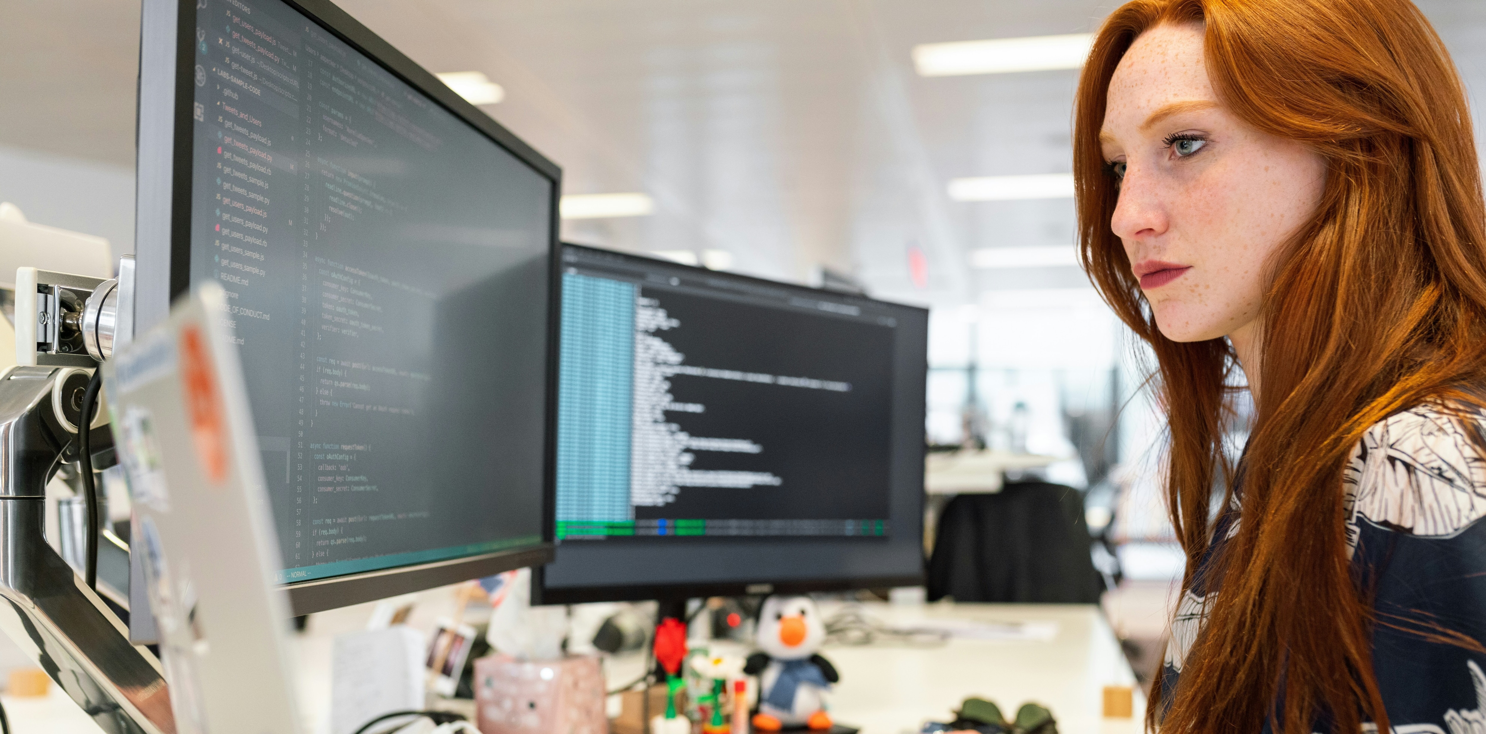 A female senior software developer looks at code on two computer monitors: Institutional knowledge of senior developers has depended on their juniors learning from them – AI has changed that