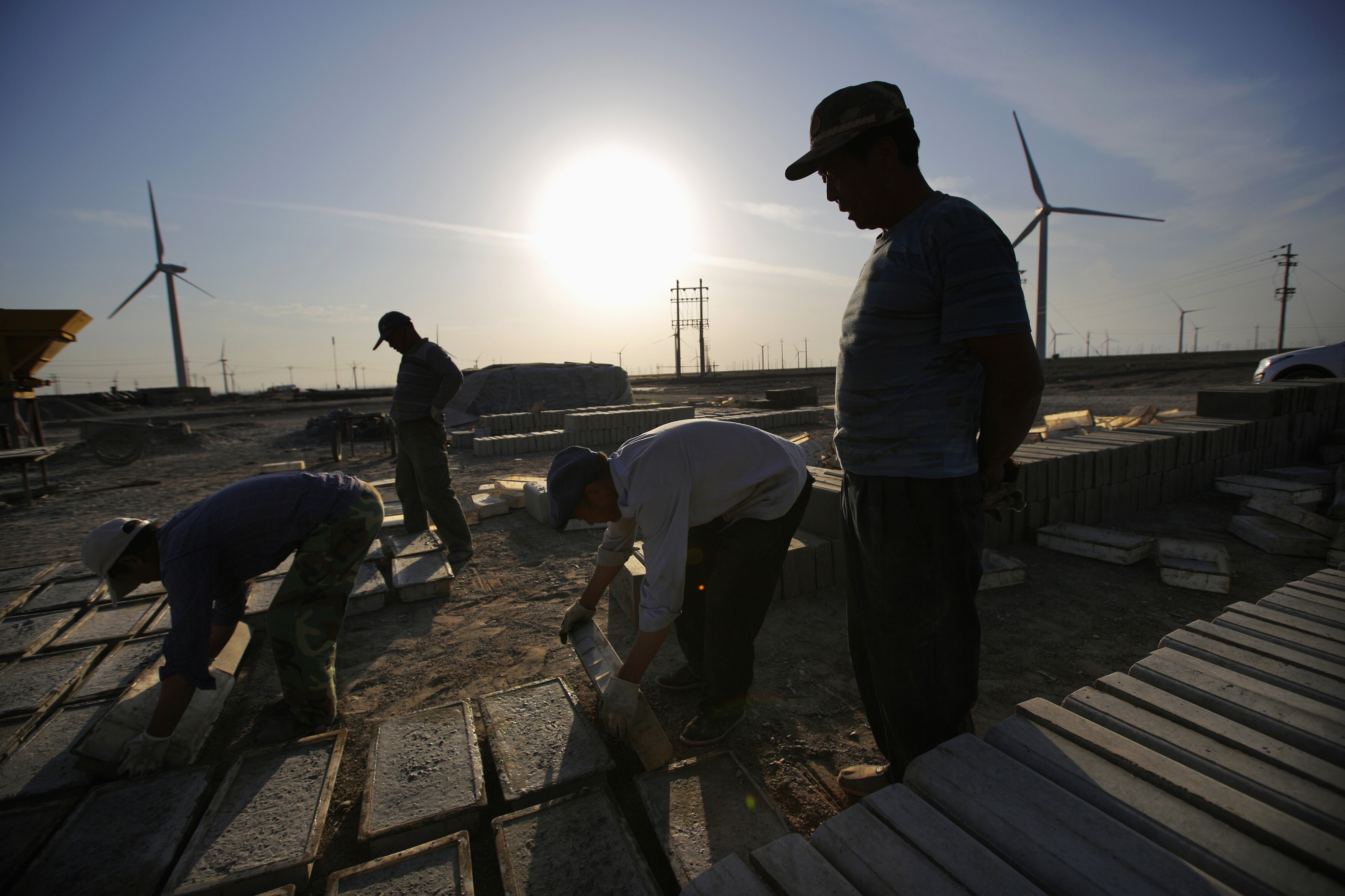 Labourers work at a construction site near wind turbines generating electricity at a wind farm in Guazhou, 950km (590 miles) northwest of Lanzhou, Gansu Province September 15, 2013. China is pumping investment into wind power, which is more cost-competitive than solar energy and partly able to compete with coal and gas. China is the world's biggest producer of CO2 emissions, but is also the world's leading generator of renewable electricity. Environmental issues will be under the spotlight during a working group of the Intergovernmental Panel on Climate Change, which will meet in Stockholm from September 23-26: Low wages reveal a structural tension at the heart of the green transition