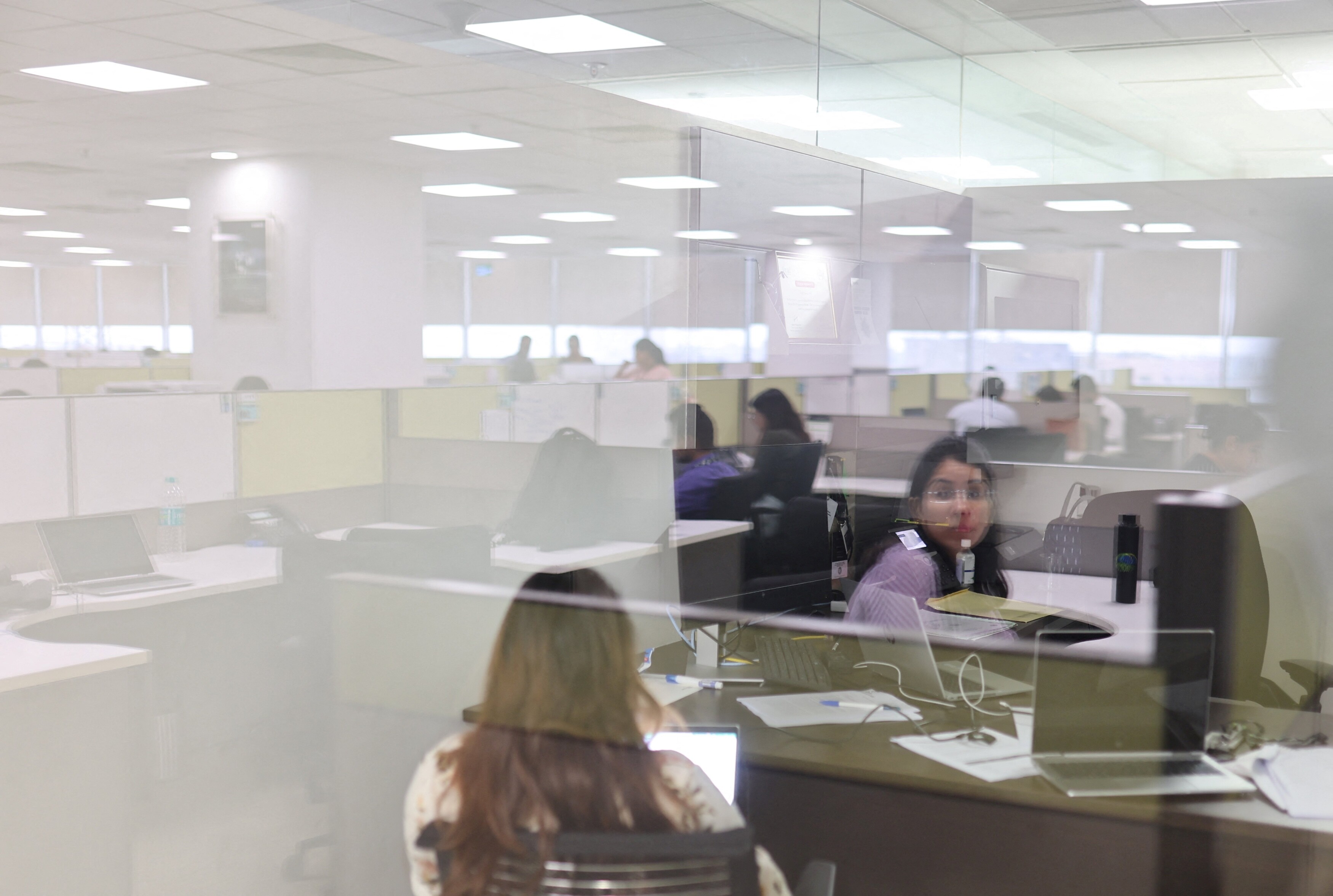 A woman is reflected on a glass as she works in a cubicle at Deloitte's office in Gurugram, India, June 13, 2023. South Asian women hold vast potential for the regional economy – but they face structural barriers to entering the workforce.