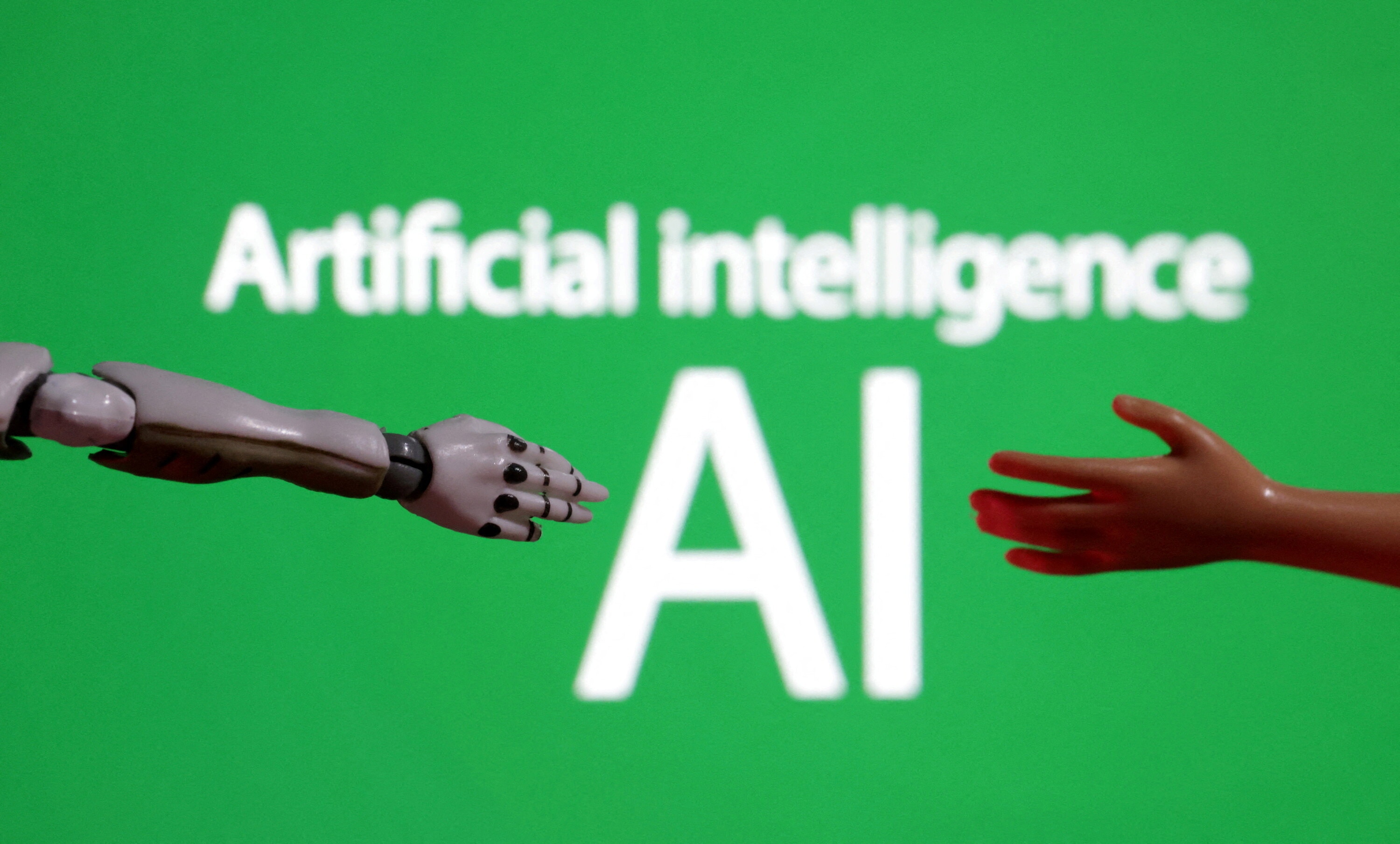 Words reading "Artificial intelligence AI", miniature of robot and toy hand are pictured in this illustration taken December 14, 2023: The next AI divide is between those who can learn the technology and those who can convert that learning into a livelihood