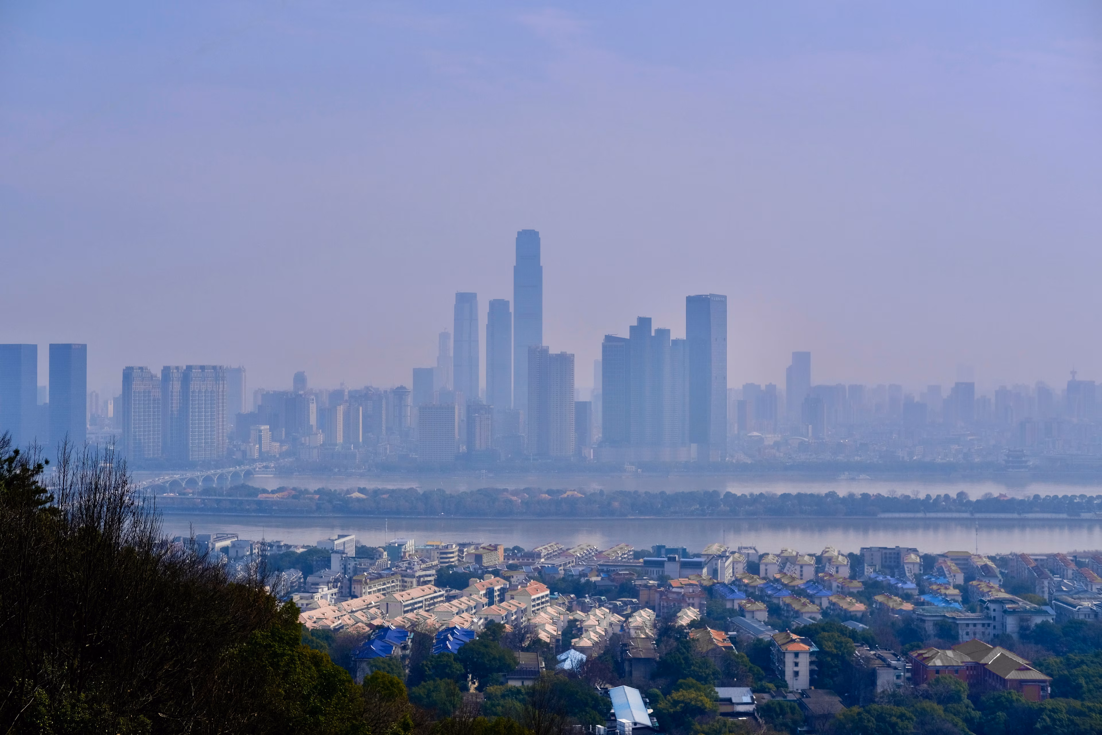 Paisaje urbano frente a un río con una inmensa capa de smog (Changsha, Hunan, China): La contaminación del aire y del agua son problemas complejos e interrelacionados que las ciudades pueden abordar de forma sistémica.
