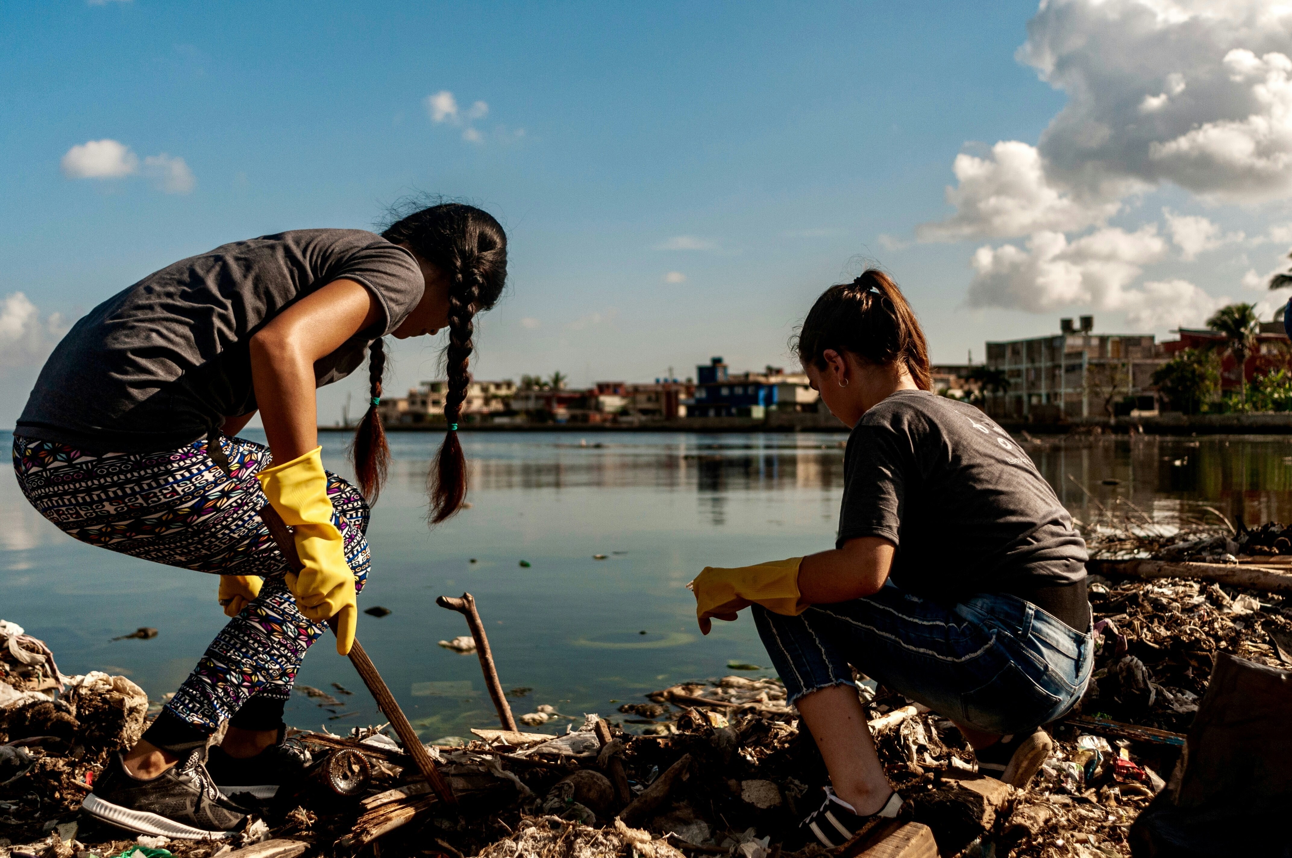 Two young girls cleaning up trash by the water: Young people closest to the harm caused by pollution are shaping solutions