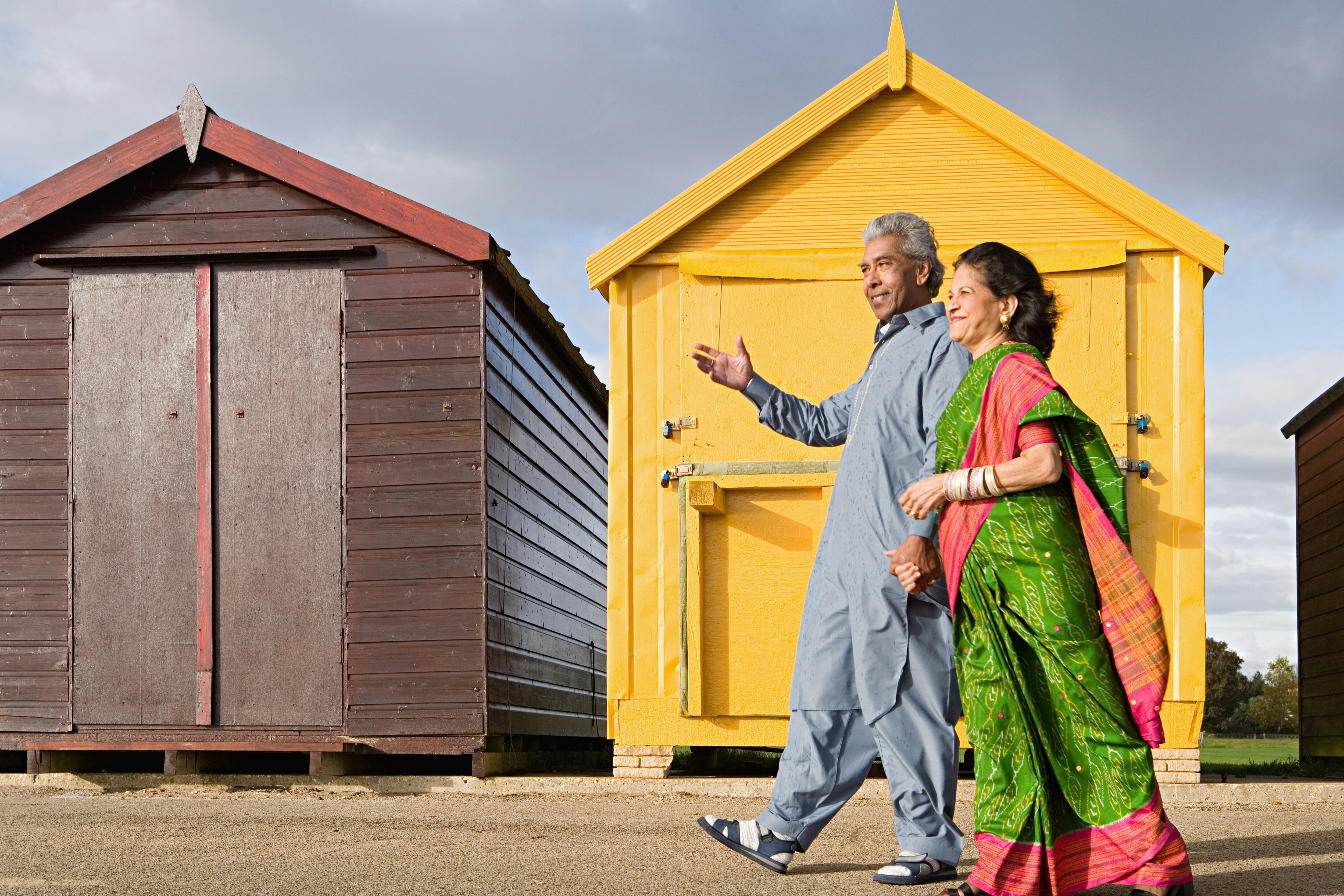 A man and women in their senior years walk past colourful beach huts: One percentage point can significant alter the trajectory of someone's retirement plan