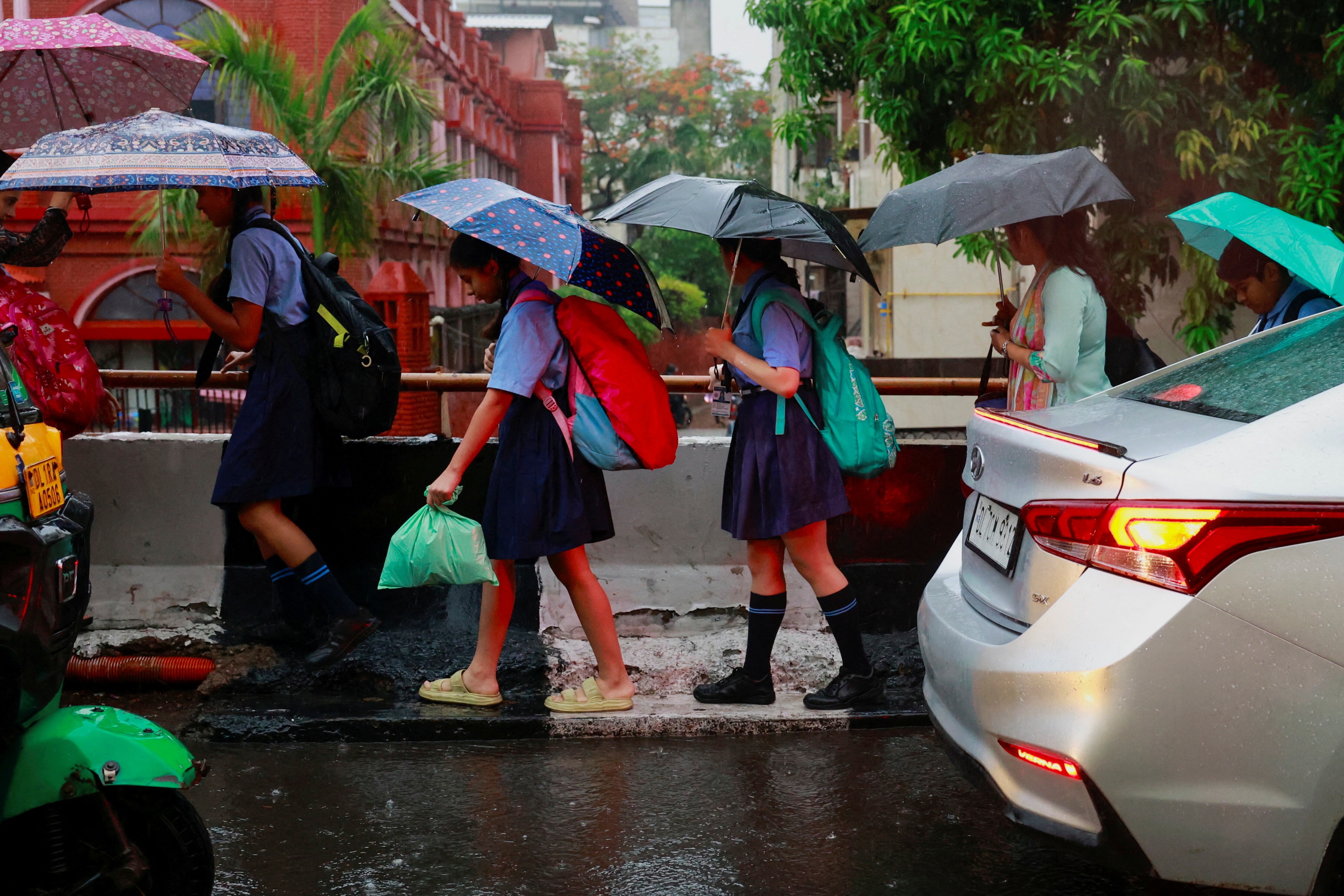 School children use umbrellas to cover themselves from the rain as they walk to school, in New Delhi, India.