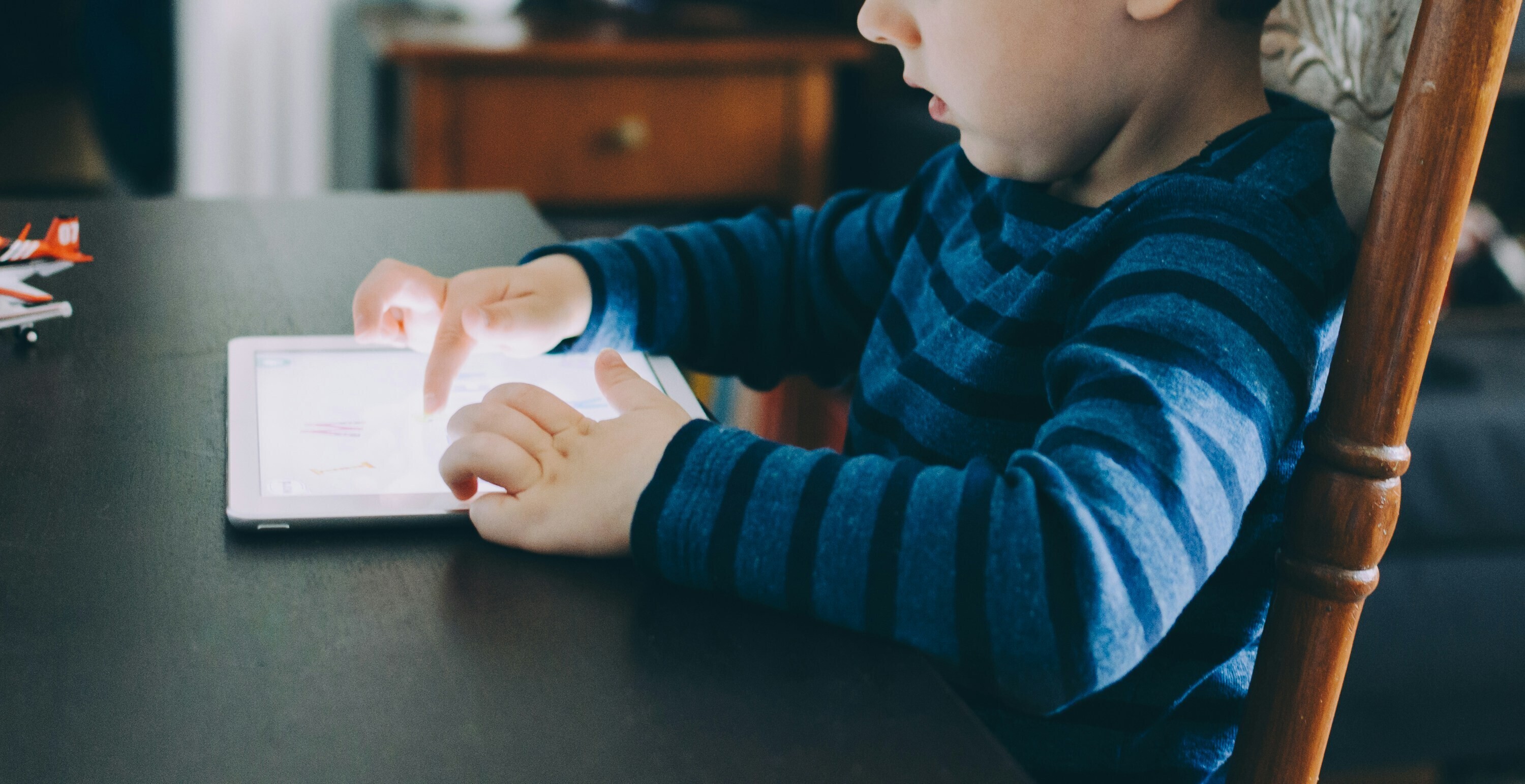 A child sits at a table using a tablet.