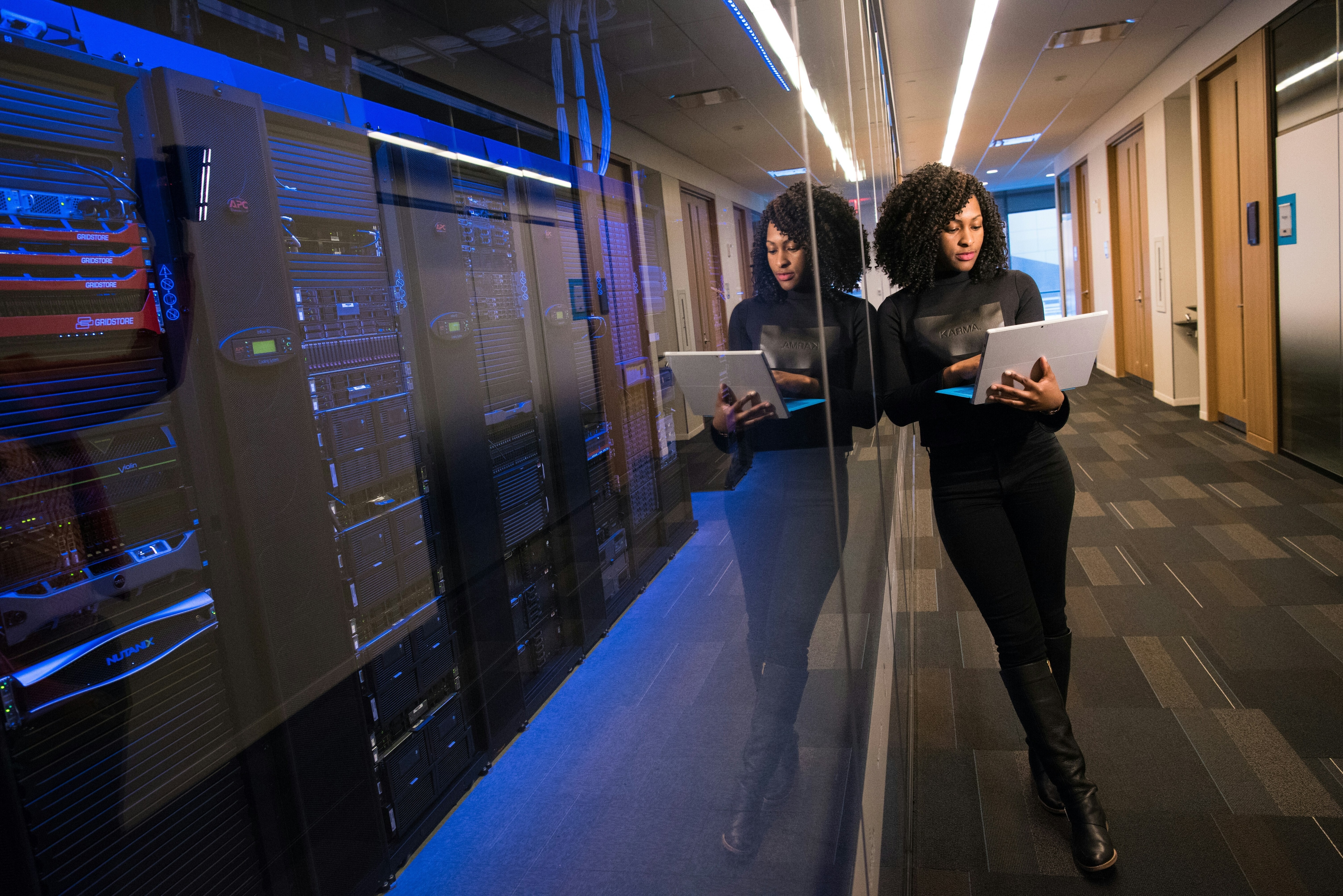A woman is on her laptop next to a server room: To bridge the cybersecurity gap, leaders must address it as a governance issue