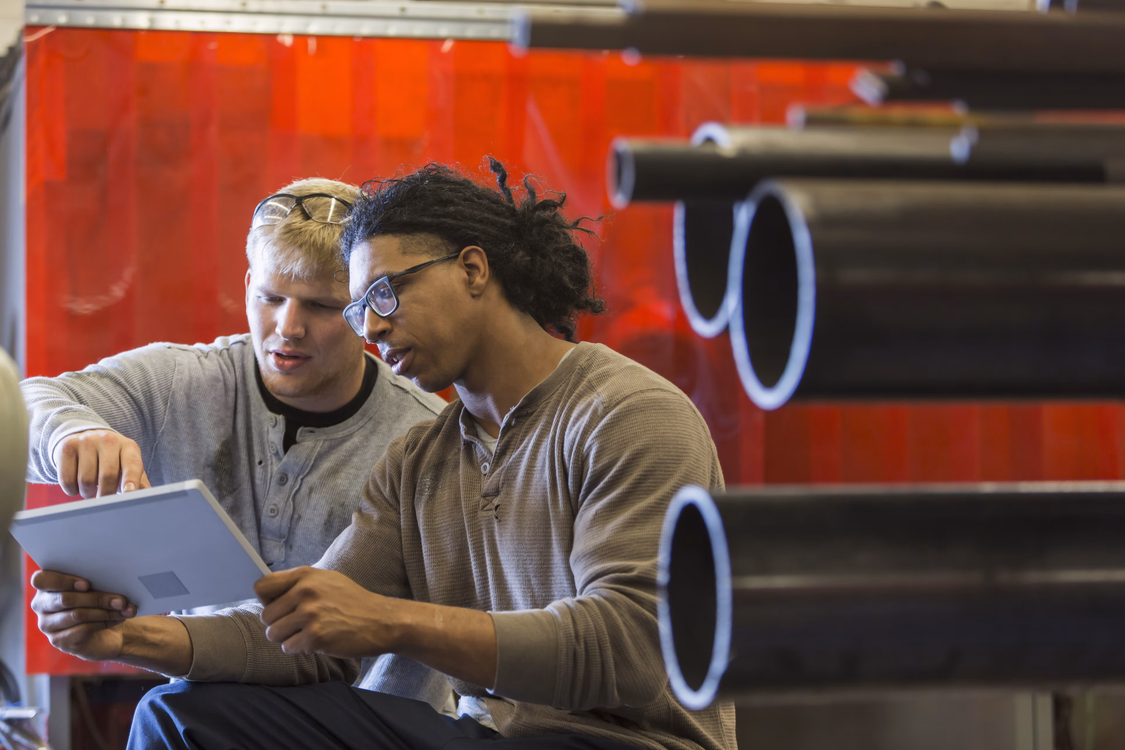 Dos hombres utilizando una tableta digital en una fábrica o taller. Uno sostiene la tableta y el otro señala la pantalla. centro de datos