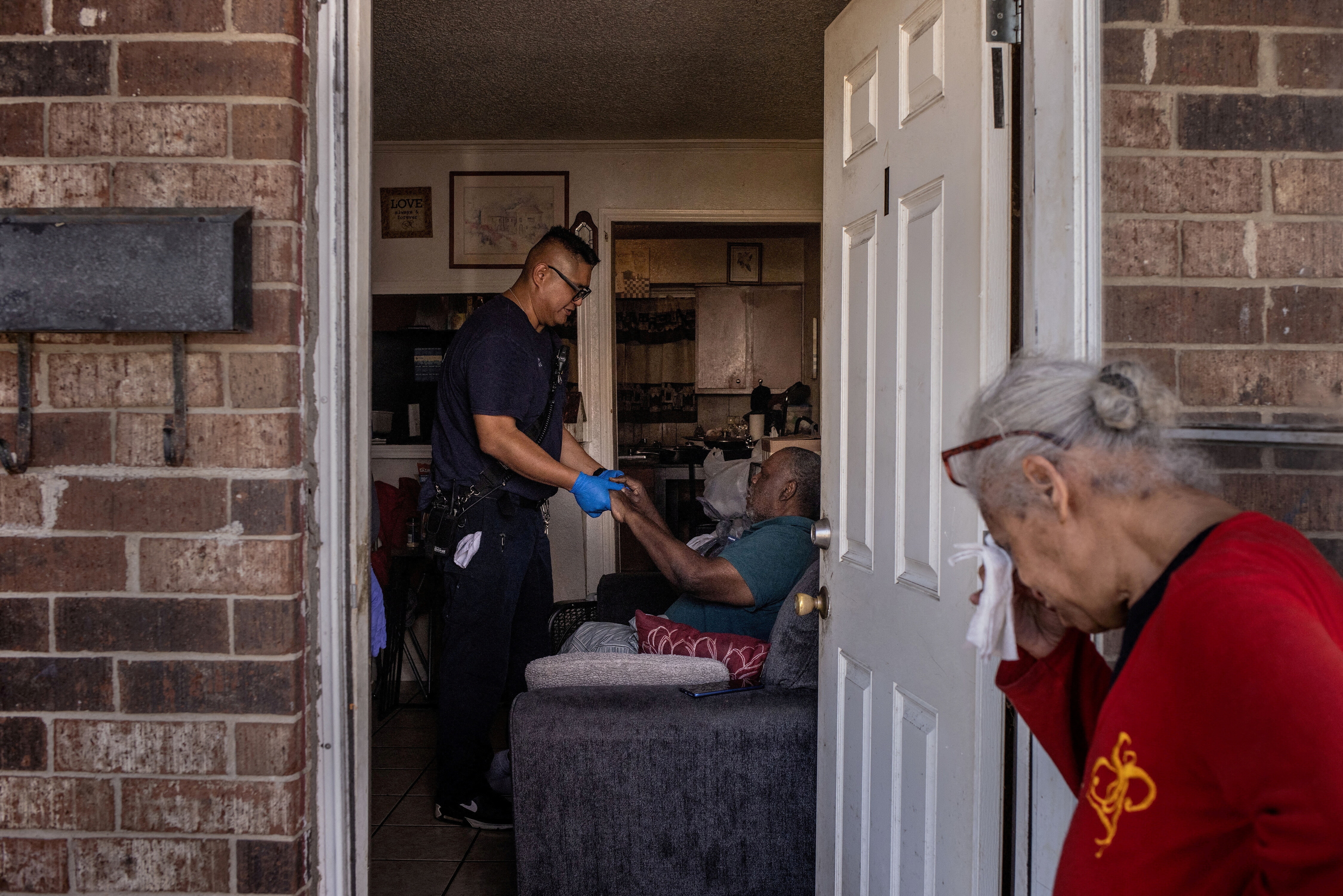 A woman reacts as a paramedic examines an older man who collapsed in his kitchen during a heat wave in Galveston, Texas.