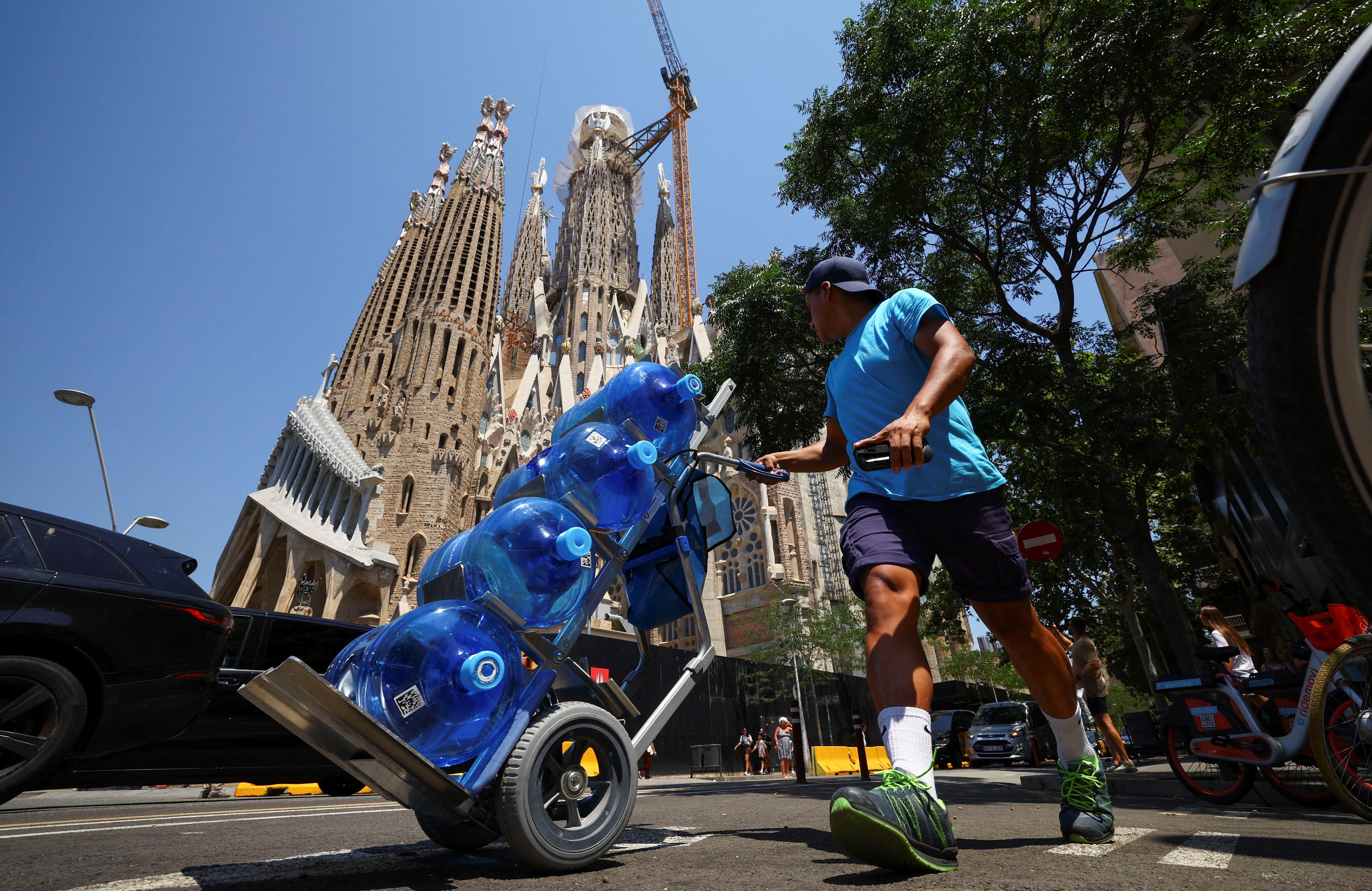 A delivery man carries water as he walks past the Sagrada Familia Basilica during a heatwave in Barcelona, Spain June 30, 2025. REUTERS/ Albert Gea