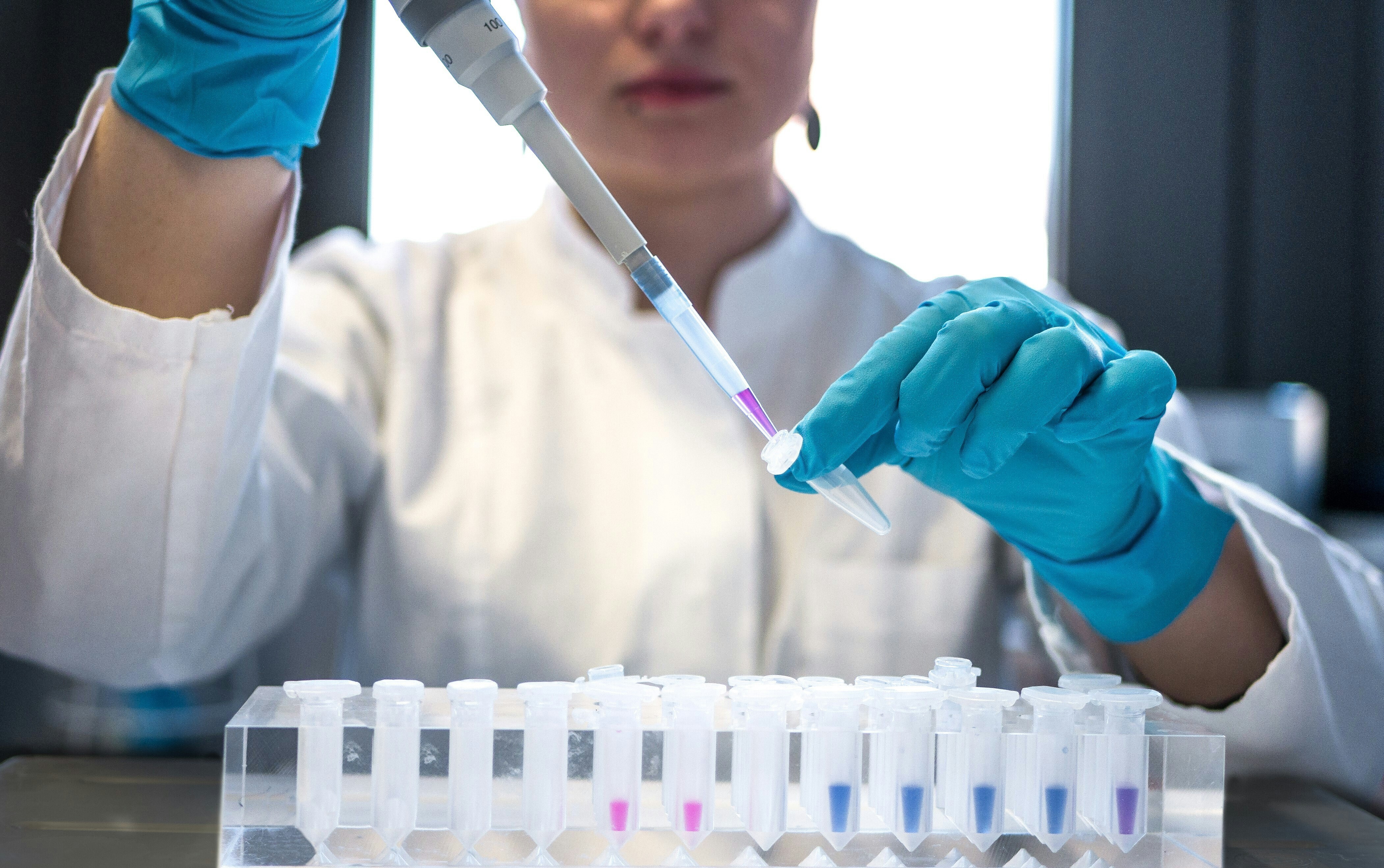 A female scientist pipetting colored chemicals into a tube.