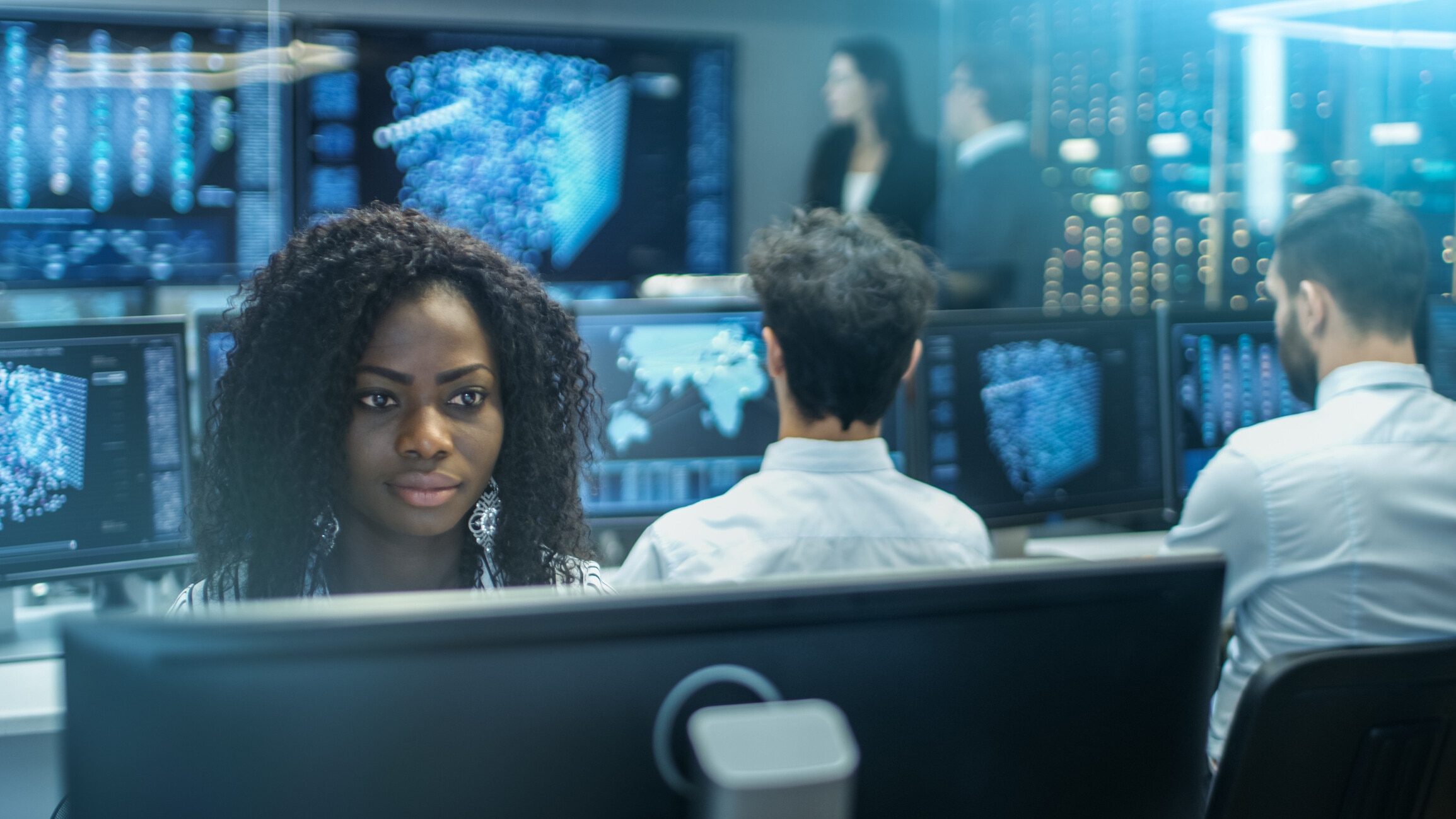 Female Computer Engineer Works on a Neural Network/ Artificial Intelligence Project with Her Multi-Ethnic Team of Specialist. Office Has Multiple Screens Showing 3D Visualization. long-term investor