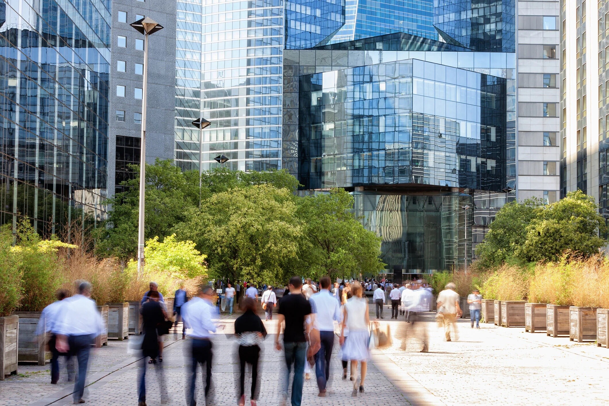 Multitud de empresarios caminando por el distrito financiero hacia un edificio de oficinas moderno, La Défense, París, Francia, ilustrando un posible precariado de la IA.