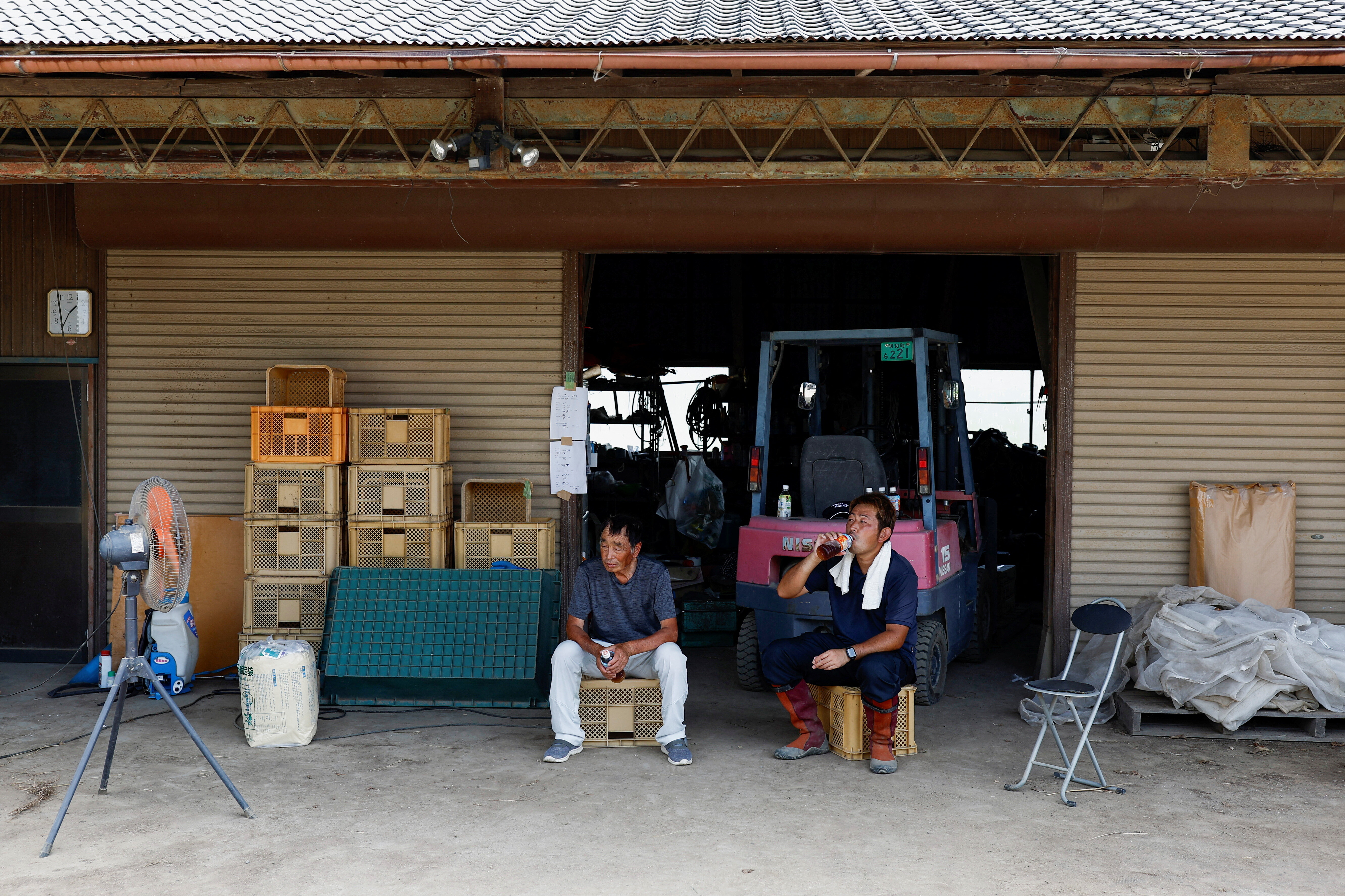 Japanese farmers Yasuyuki Kurosawa, 77, along with his son Yukihiro, 39, rest at their storage during a hot summer day in Meiwa, Gunma prefecture, Japan, August 7, 2024.