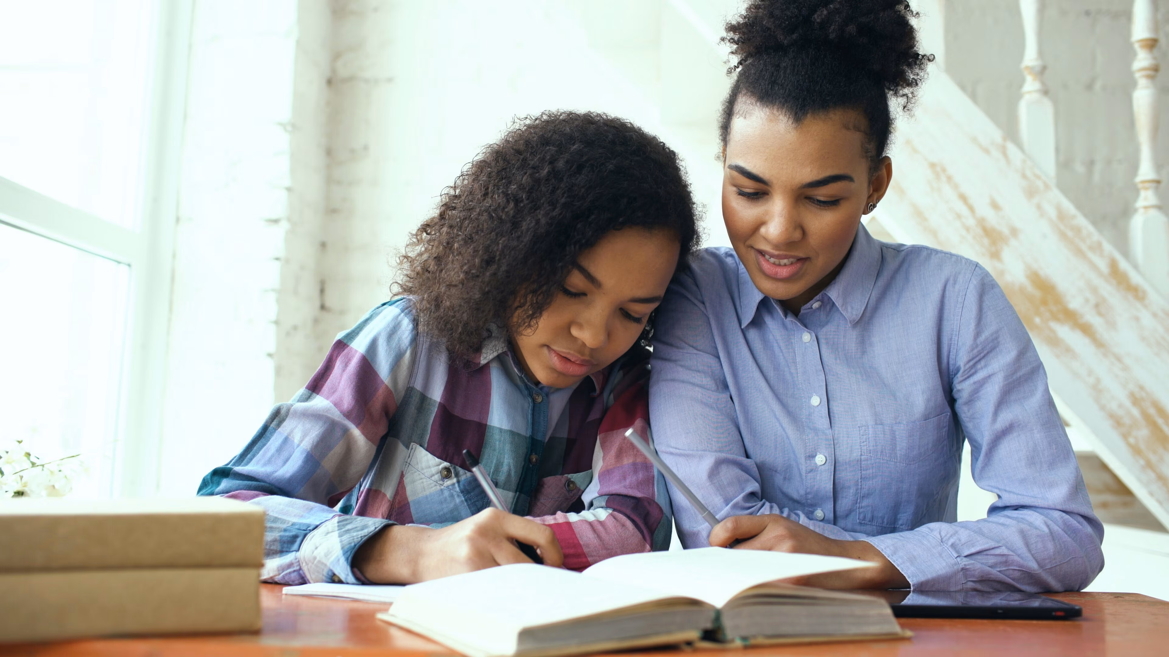 Una madre y su hija adolescente conversan relajadas mientras trabajan juntas con una laptop en casa.