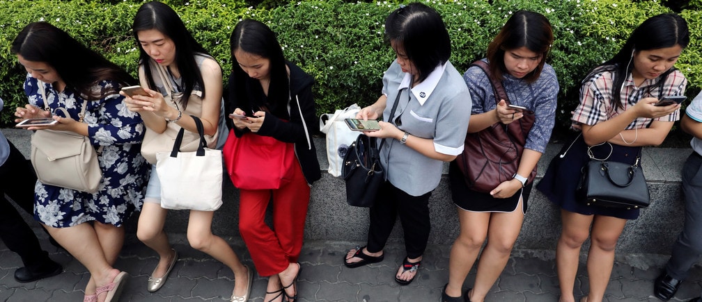 Women use their mobile phones while waiting for a bus at rush hour in Bangkok, Thailand October 4, 2018. REUTERS/Jorge Silva - RC150B3A10D0