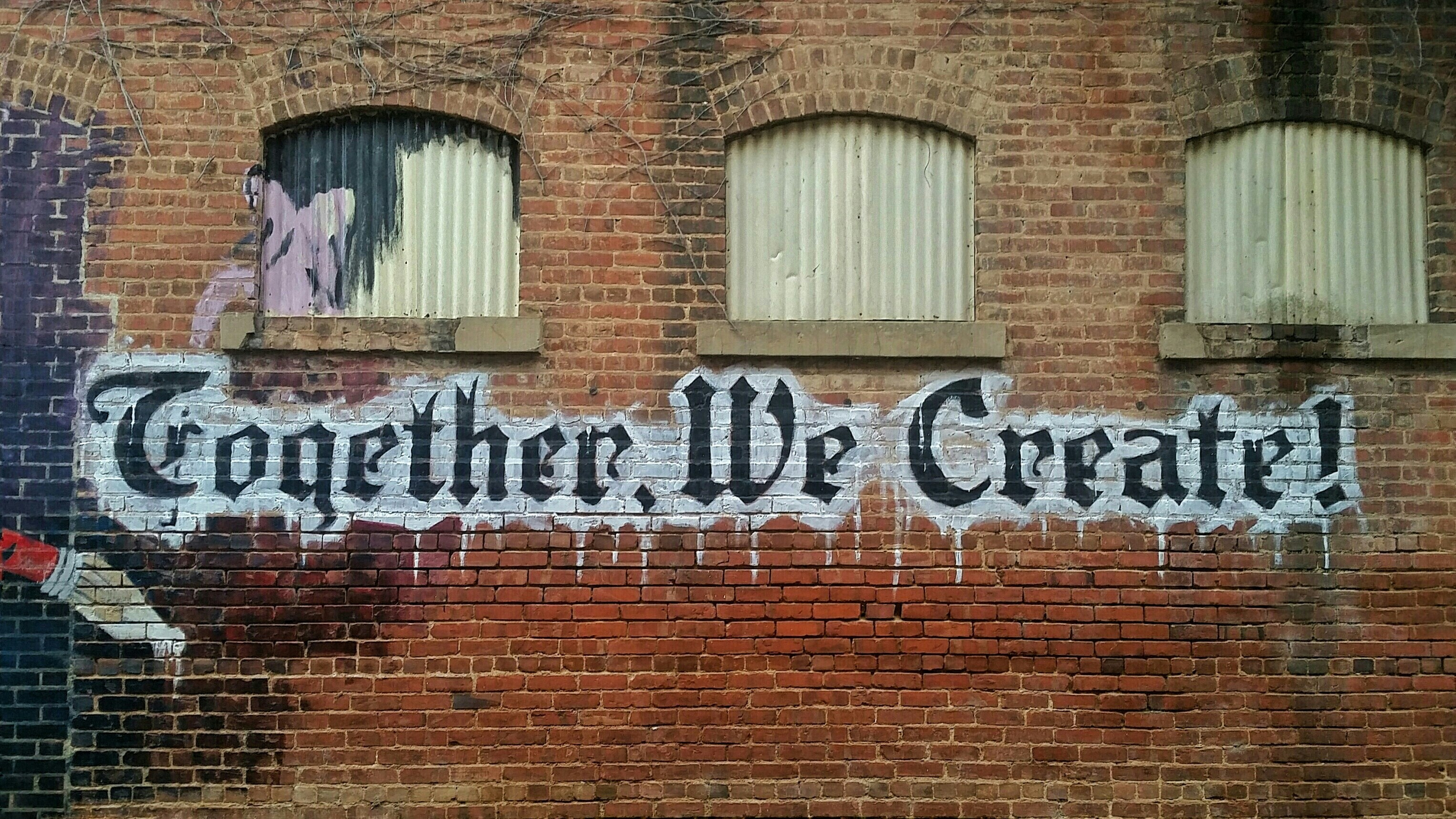 “Together, we create!” graffiti on brick wall with pen nib.