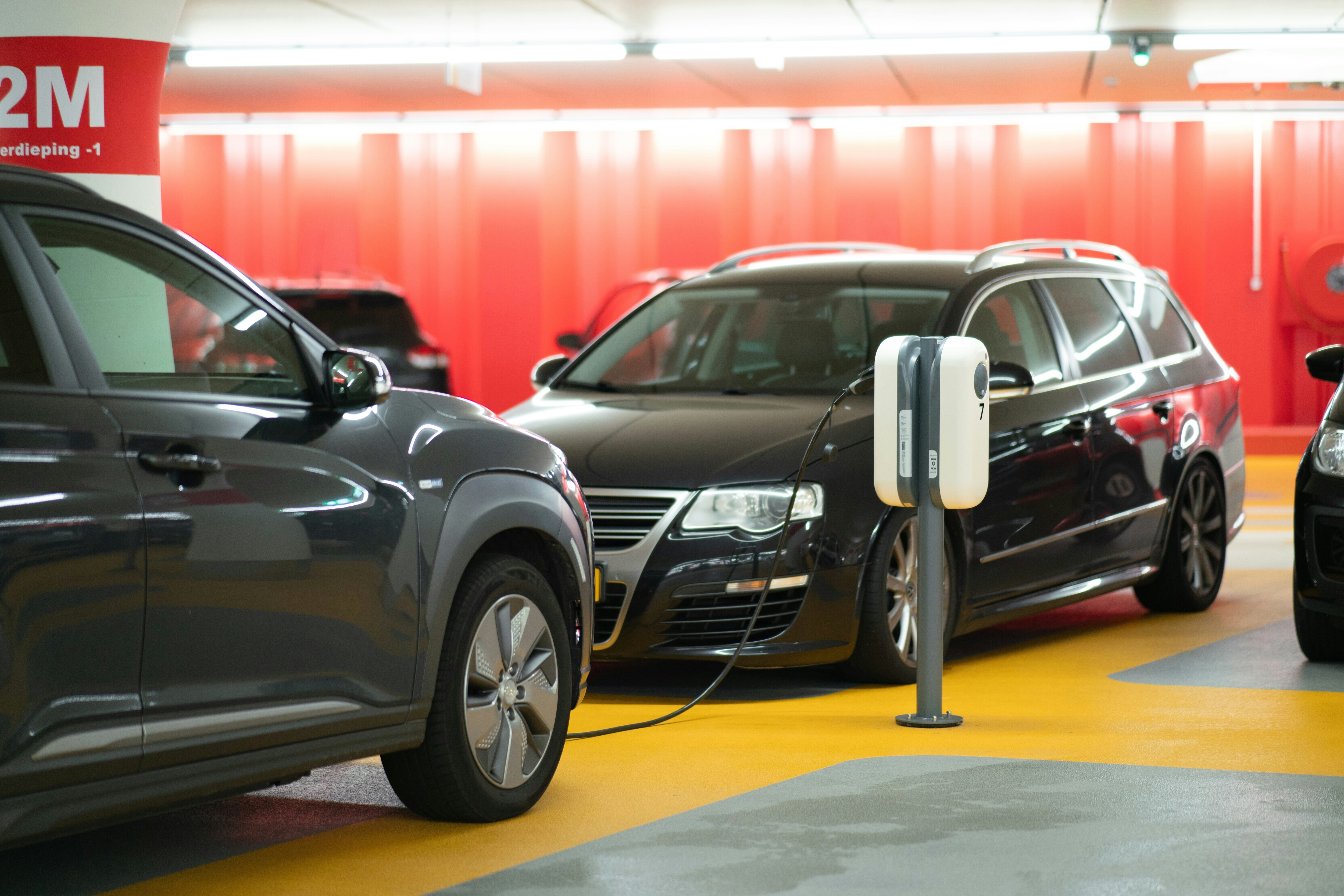 Two black cars by an electric charge point in a car park with yellow floor markings and red walls: Electrification's benefits are becoming self-propelling