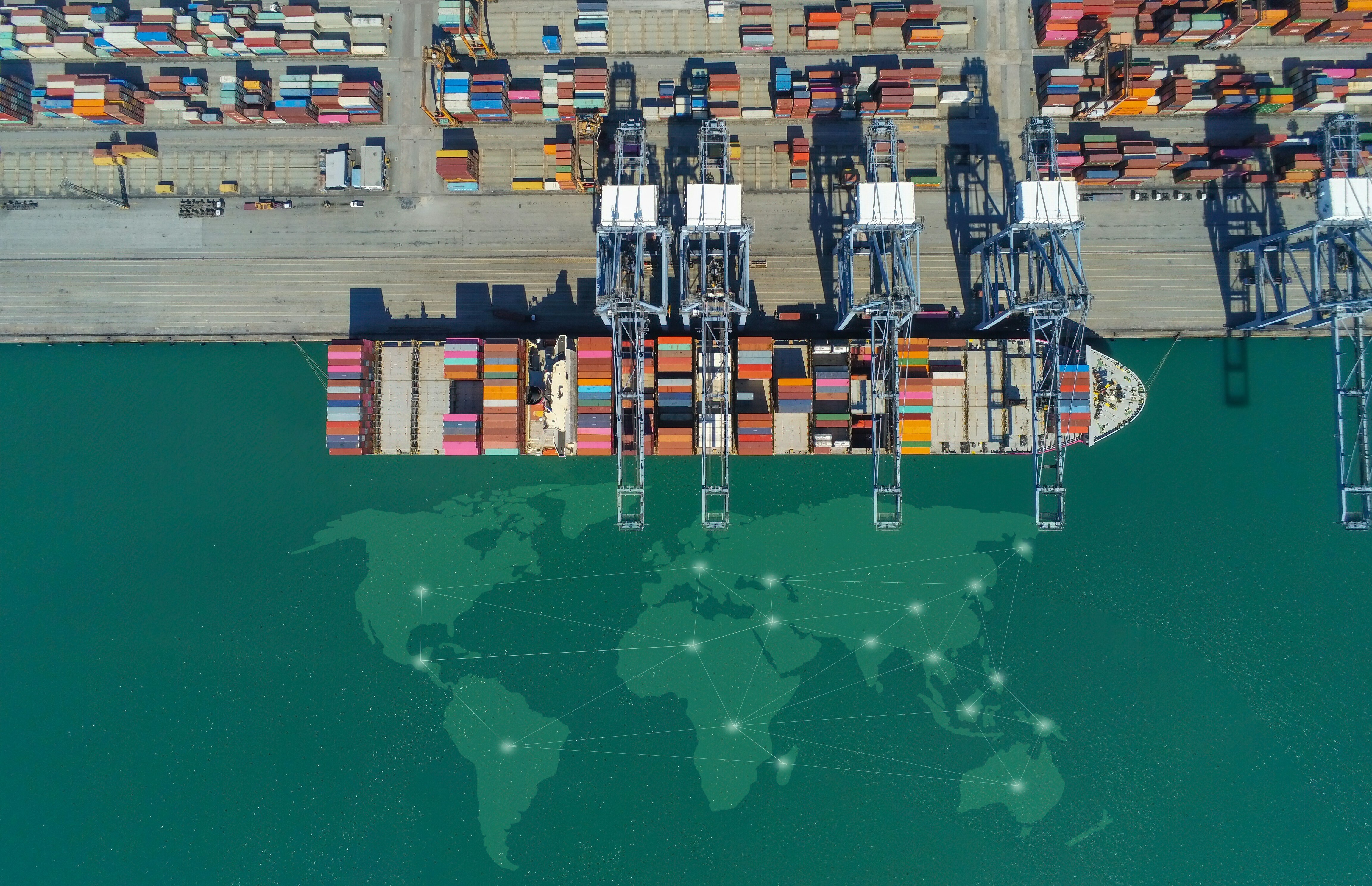 Aerial view of a container ship at a port with a global map overlay representing international trade data