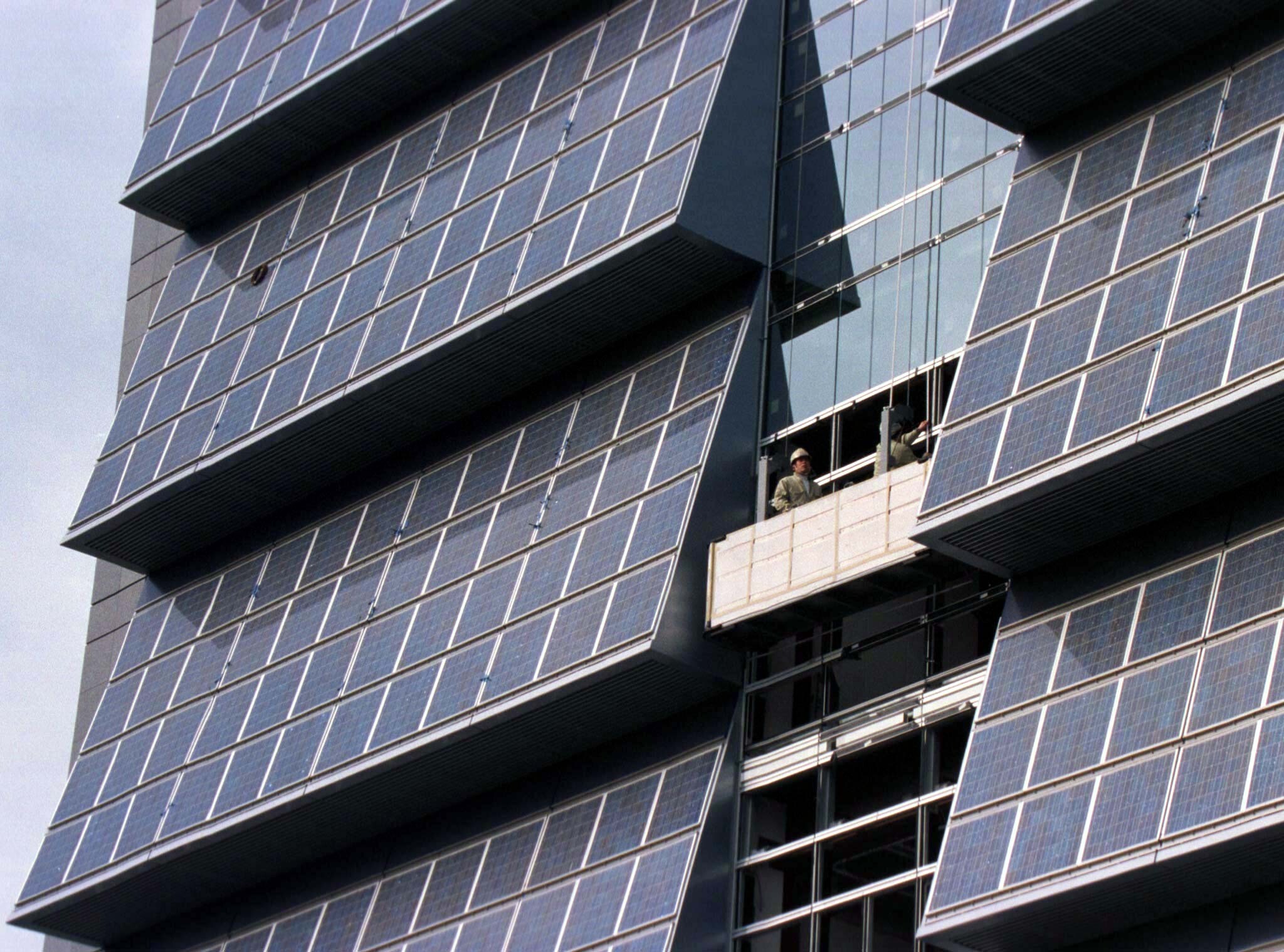 Between some 1,392 solar panels, workers are lowered along the outside wall of a 20-floor building, Kyocera Corporation's new environment-conscience solar-paneled headquarter building currently under construction in Japan's ancient capital of Kyoto December 1, where a crucial global warming conference has opened. The structure is 95 metres tall and has the world's largest solar system along a vertical wall, the company said. The building is due for completion in summer 1998: Government support is accelerating green materials development in Japan