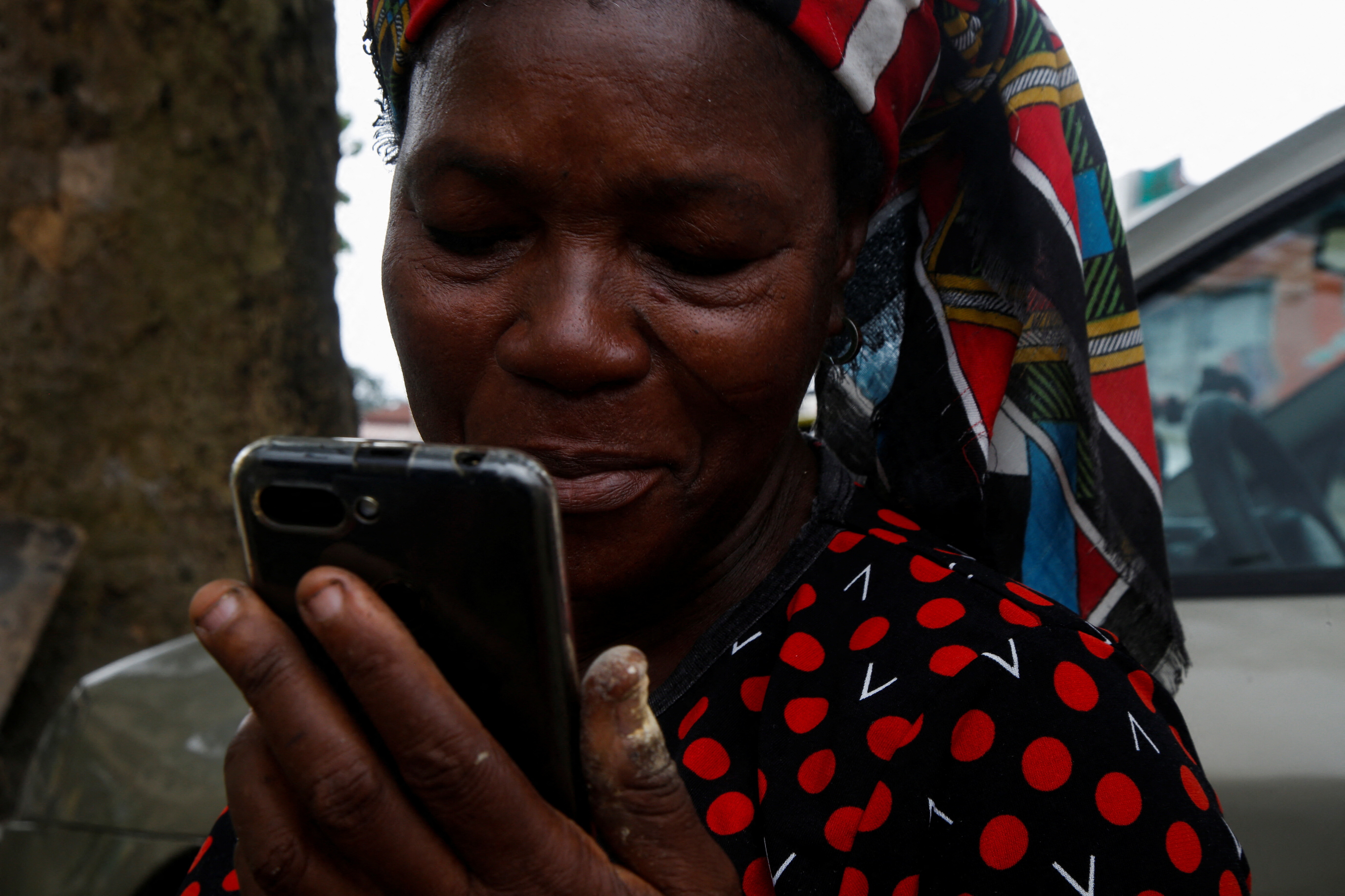 Madeleine Zoundi, 45, a street vendor, smiles as she hears her local language through the Open G smartphone, which can speak local Ivorian languages, at a shop in Abidjan, Ivory Coast  August 12, 2022. REUTERS/Luc Gnago. govtech