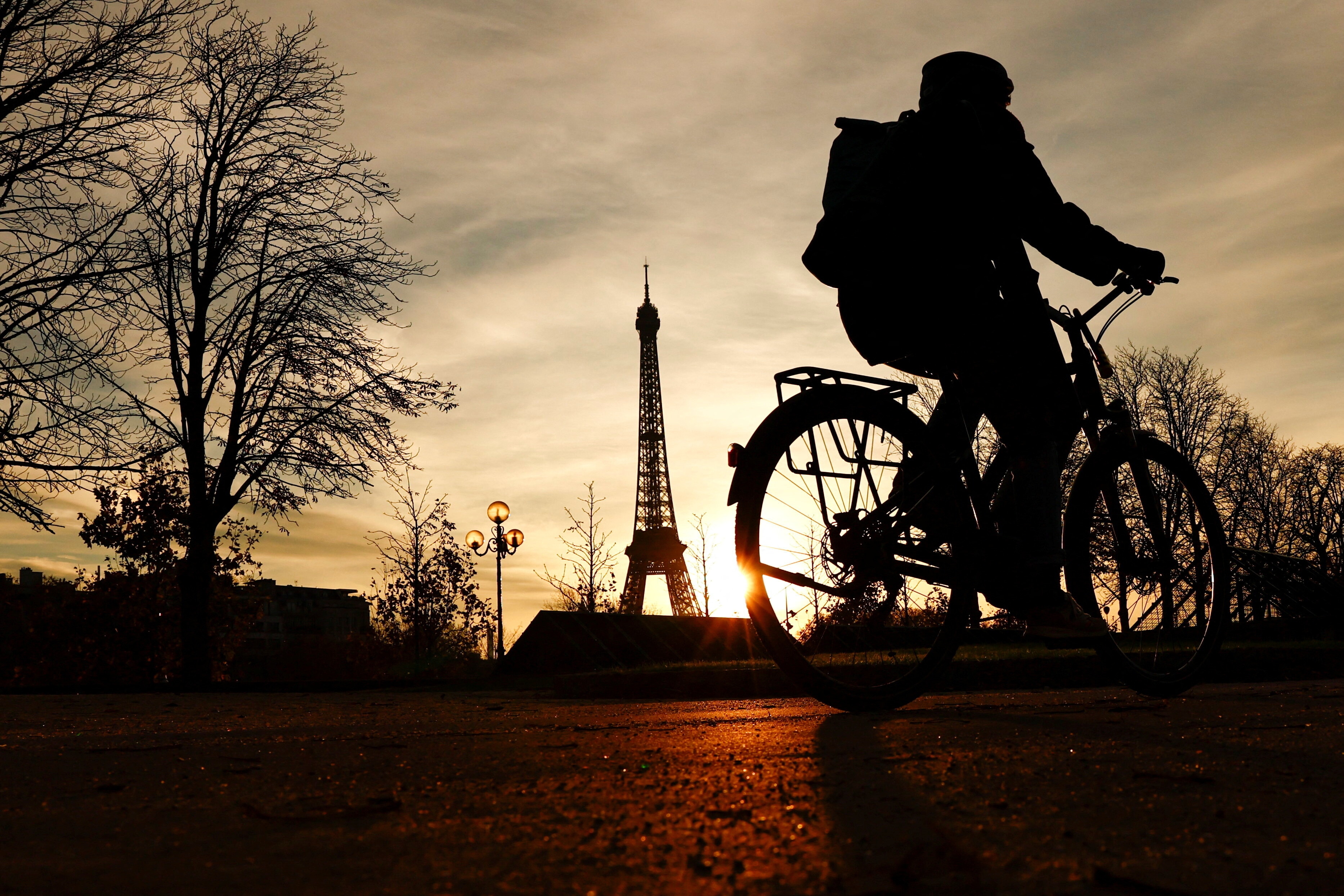 A woman rides her bicycle along the banks of the River Seine near the Eiffel Tower at sunset in Paris France, November 22, 2023: Cities need the right mix of talent, venture capital, mobility infrastructure and climate resilience to appeal to multinationals