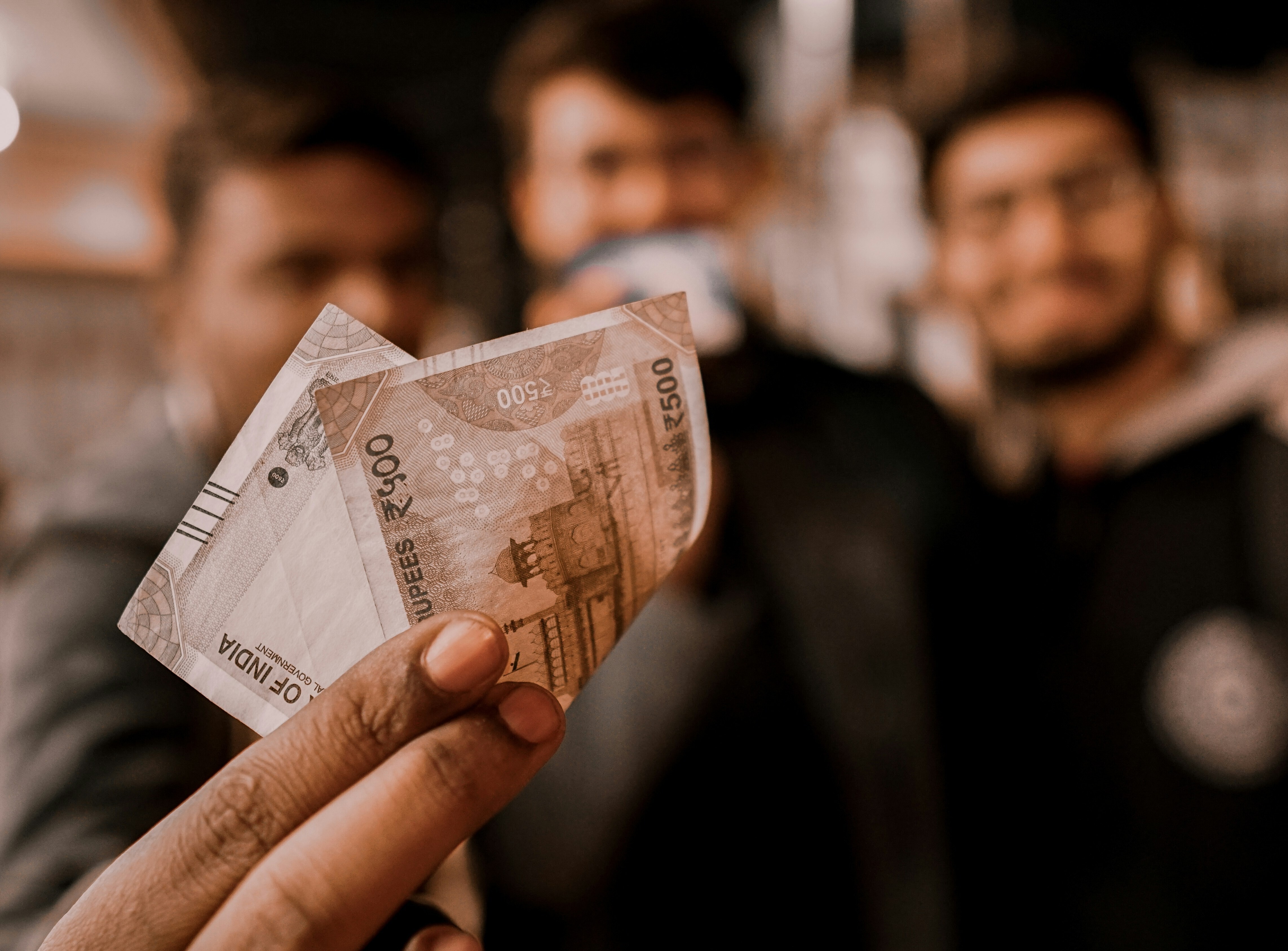 A man holds up Indian rupees with two other men in the background: Proof of concept for tokenized bonds exists around the world