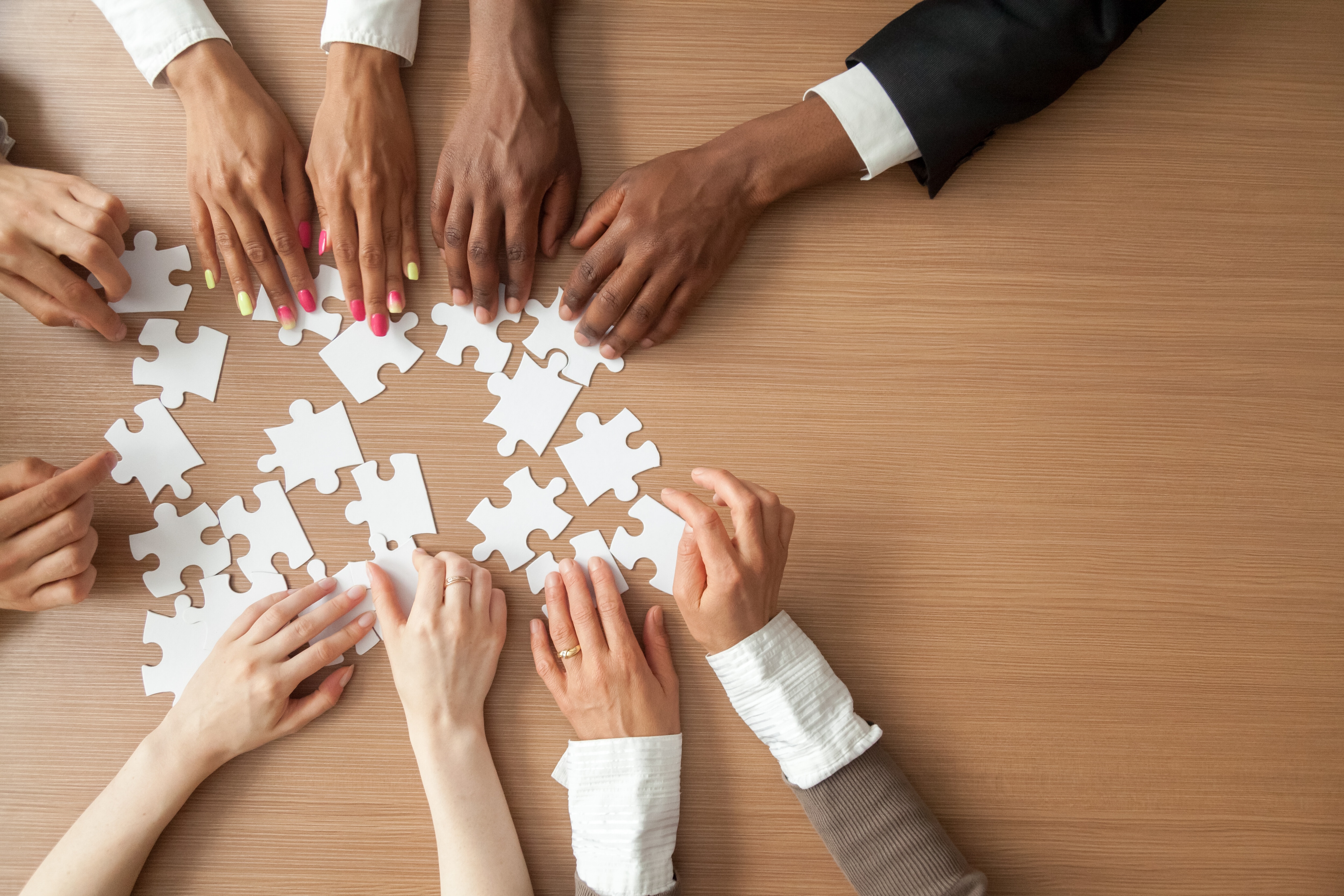 Hands of multi-ethnic team assembling jigsaw puzzle, multiracial group of black and white people joining pieces at desk, successful teamwork concept, help and support in business, close up top view. Workforce
