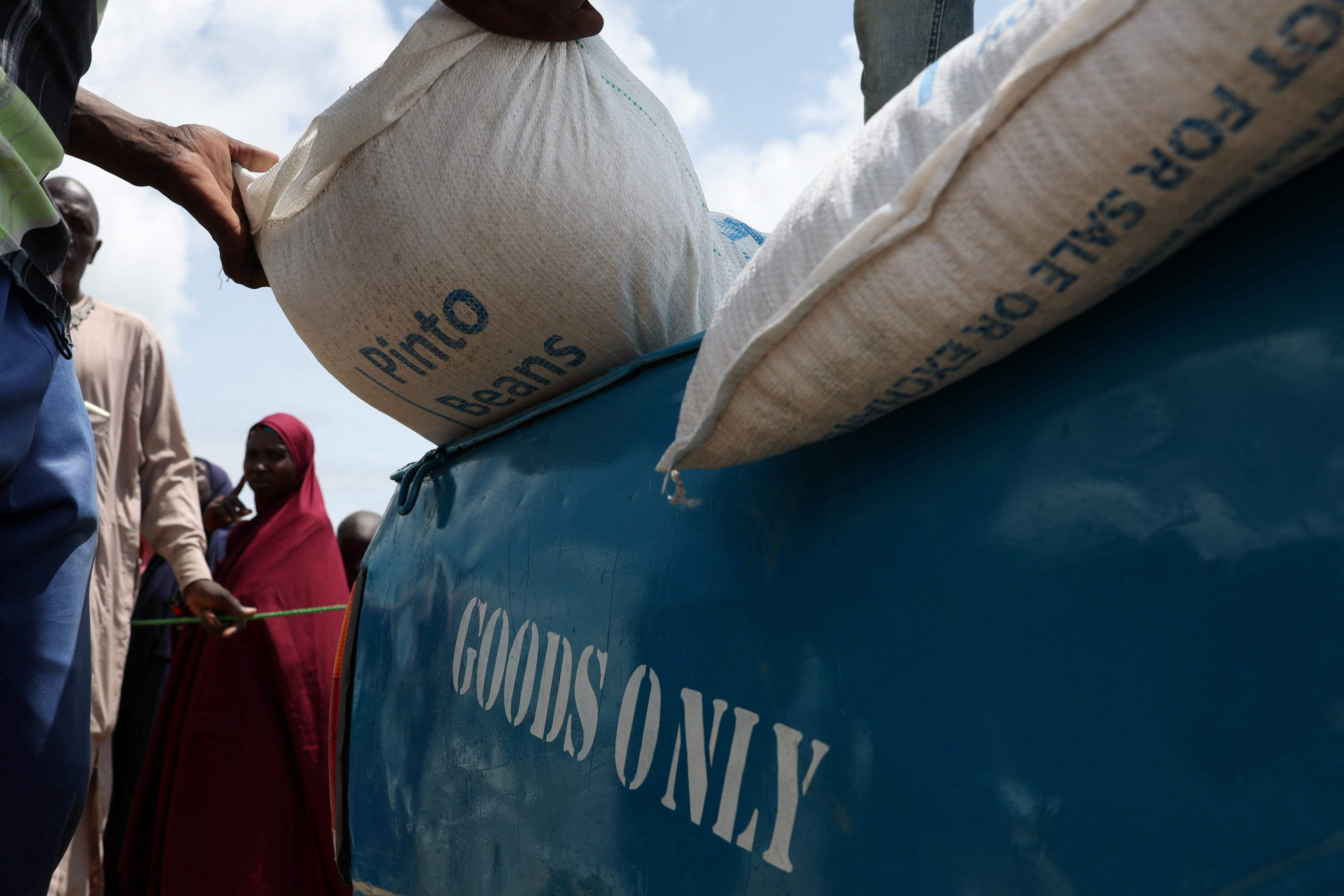 Camp workers offload bags of pinto beans near an open field as beneficiaries from different Internally Displaced Persons camps wait to receive support following the exit of USAID, at a World Food Programme distribution centre in Dikwa, Borno State, Nigeria, August 27, 2025. REUTERS/Sodiq Adelakun.