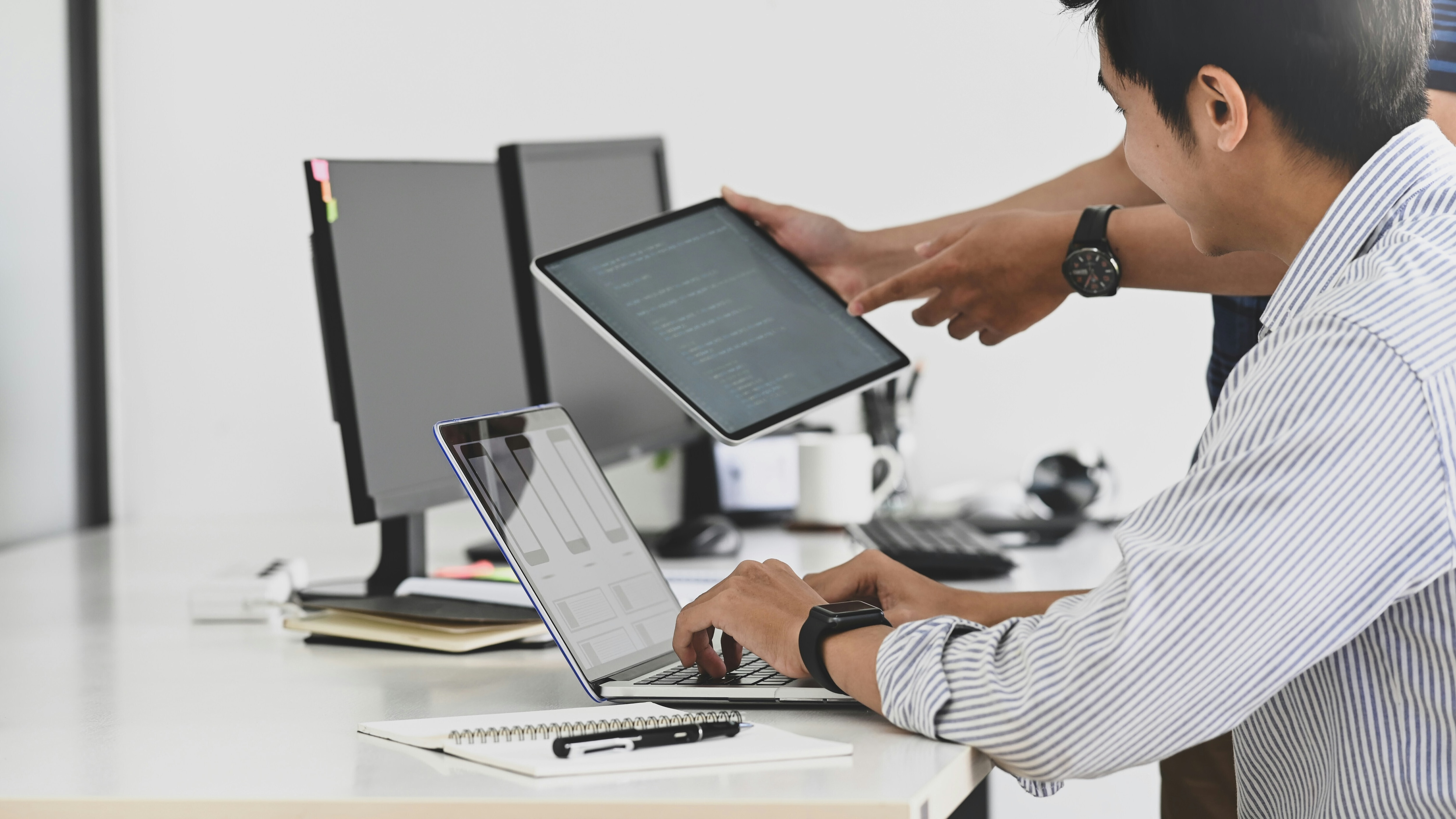 A man in a pin stripe shirt surrounded by several devices and a colleague pointing to an iPad: Early action is critical if ICT decarbonization is to deliver results