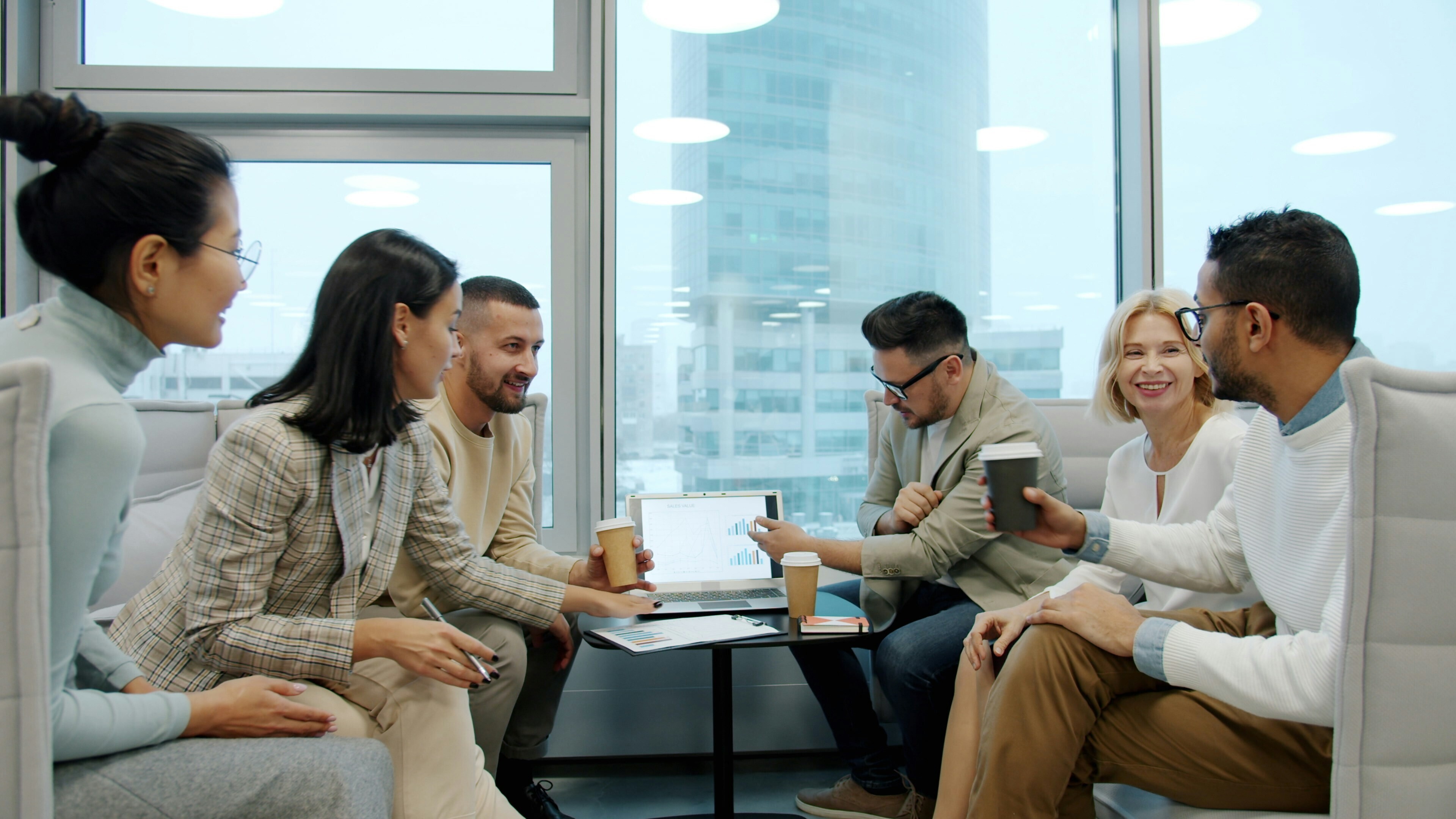 A group of young professionals are working around a laptop while drinking coffee.