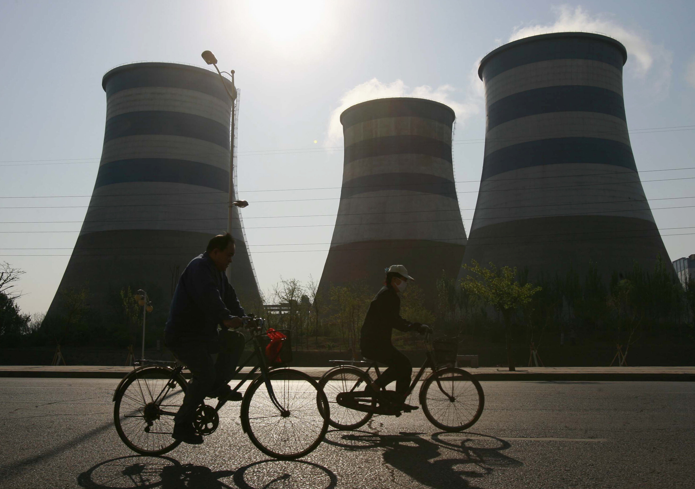 Local residents cycle past chimneys at a steel factory in Shenyang, northeast China's Liaoning province, May 3, 2007: “Crocodile economics” shows growth and climate progress can occur.